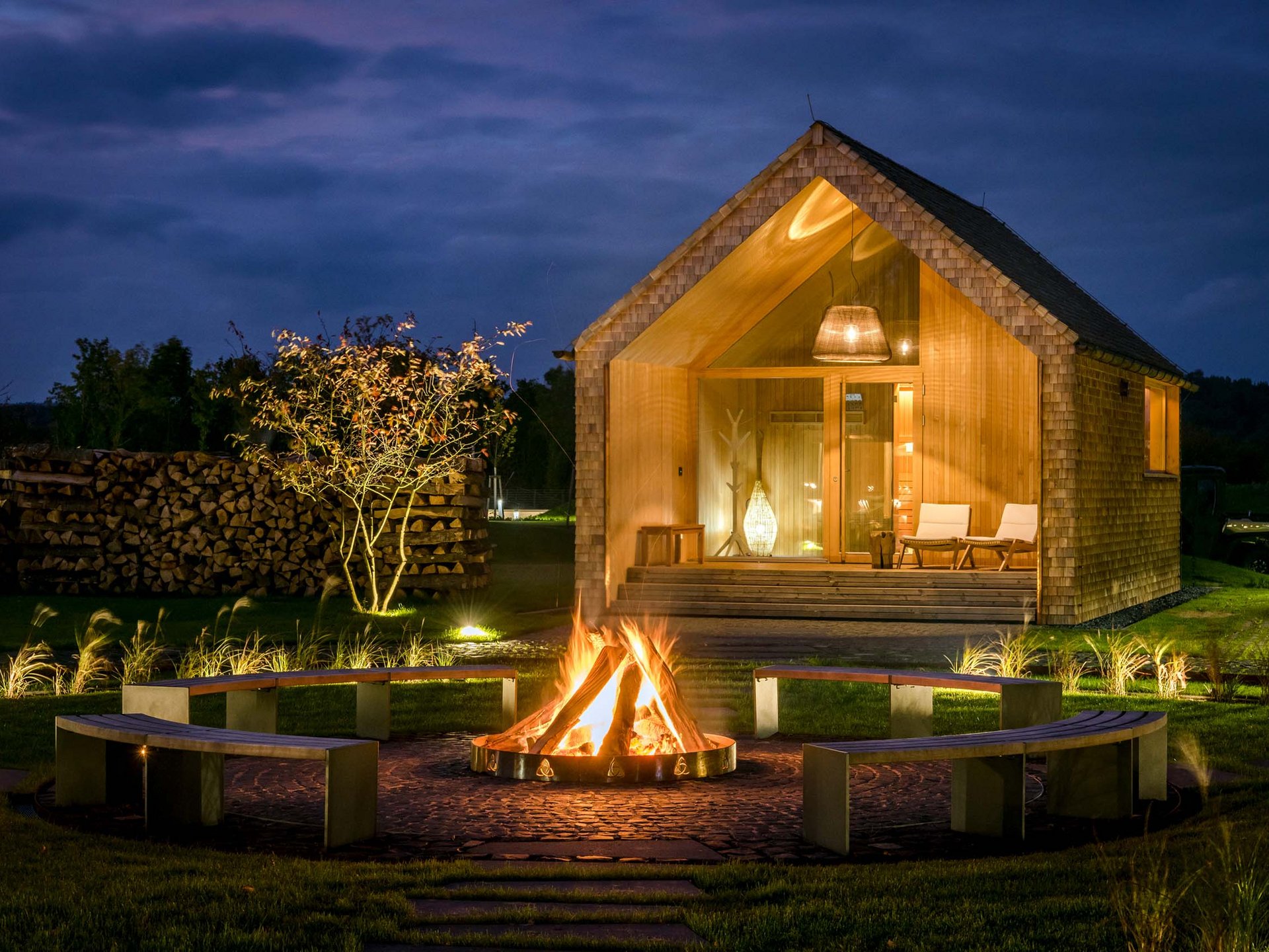 Wooden cabin at night with campfire and benches in the garden