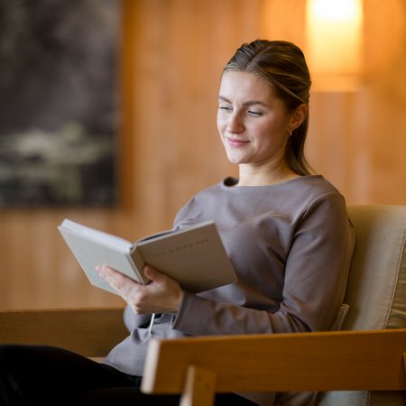 Frau liest entspannt Buch in gemütlichem Sessel zu Hause