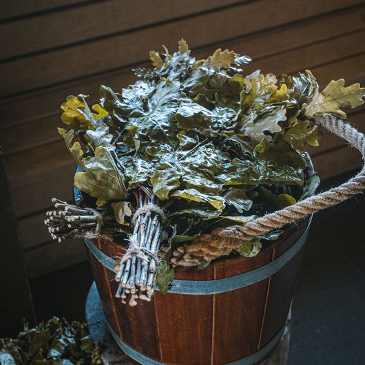 Wooden bucket with fresh oak leaf bundles in a sauna room