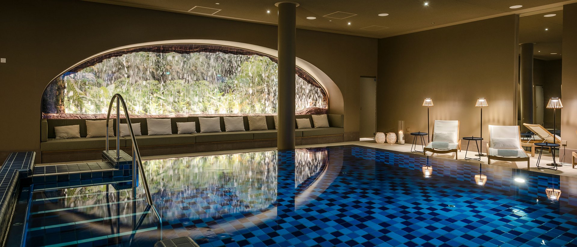 Piscine intérieure chauffée avec cascade et fauteuils lounge éclairés chaleureusement