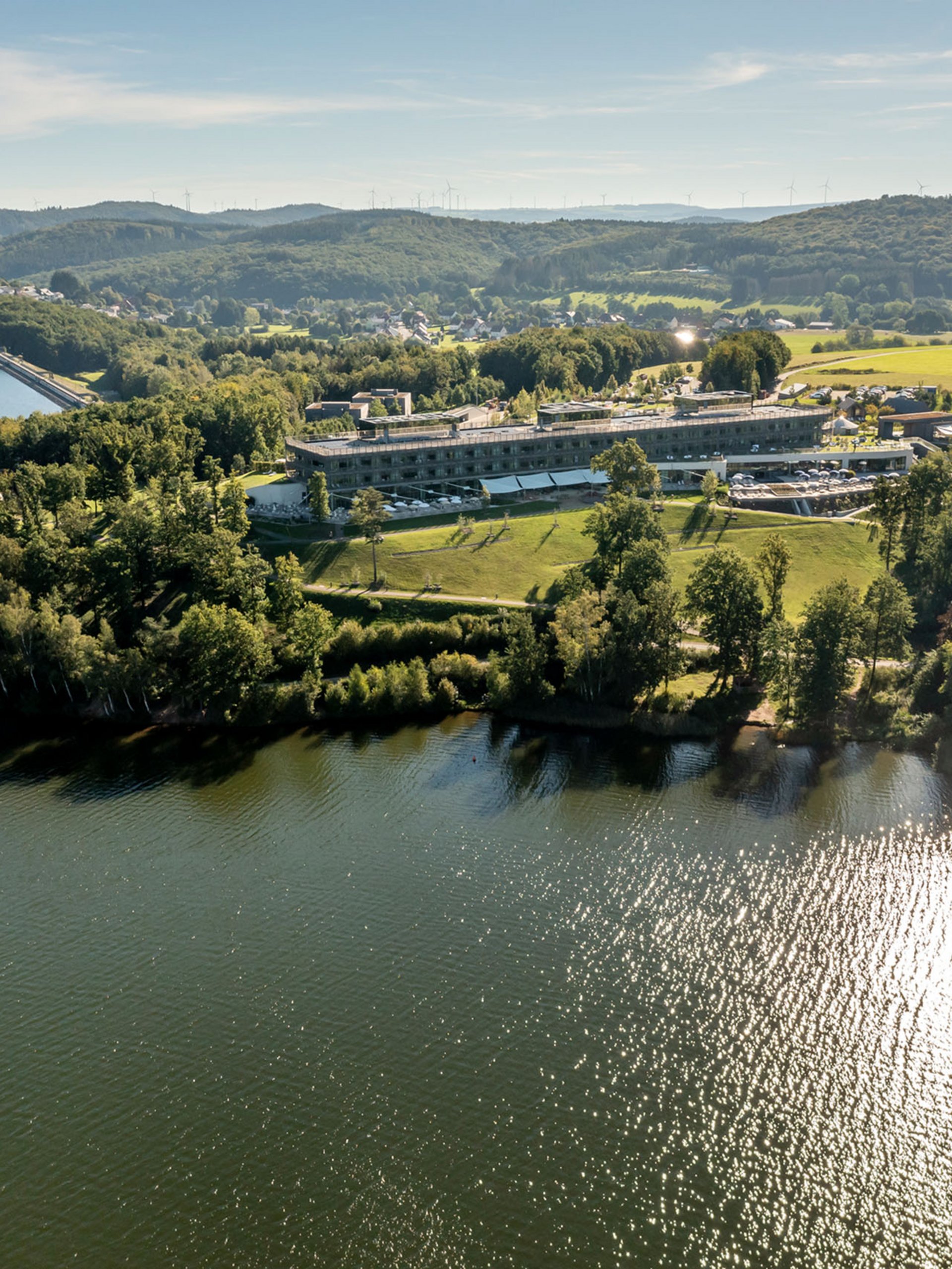 Luftaufnahme von einem See mit einem Gebäude und bewaldeten Hügeln im Hintergrund
