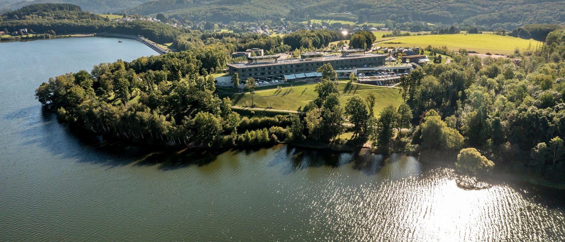 Vue aérienne d'un lac avec un bâtiment et des collines boisées en arrière-plan