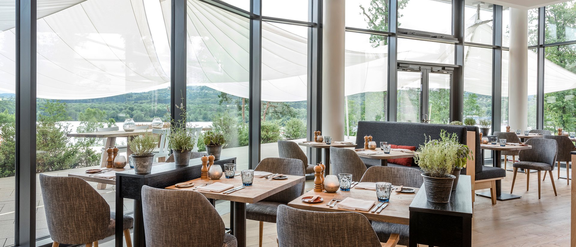 Salle de restaurant moderne avec parquet, tables et chaises, grandes fenêtres et vue