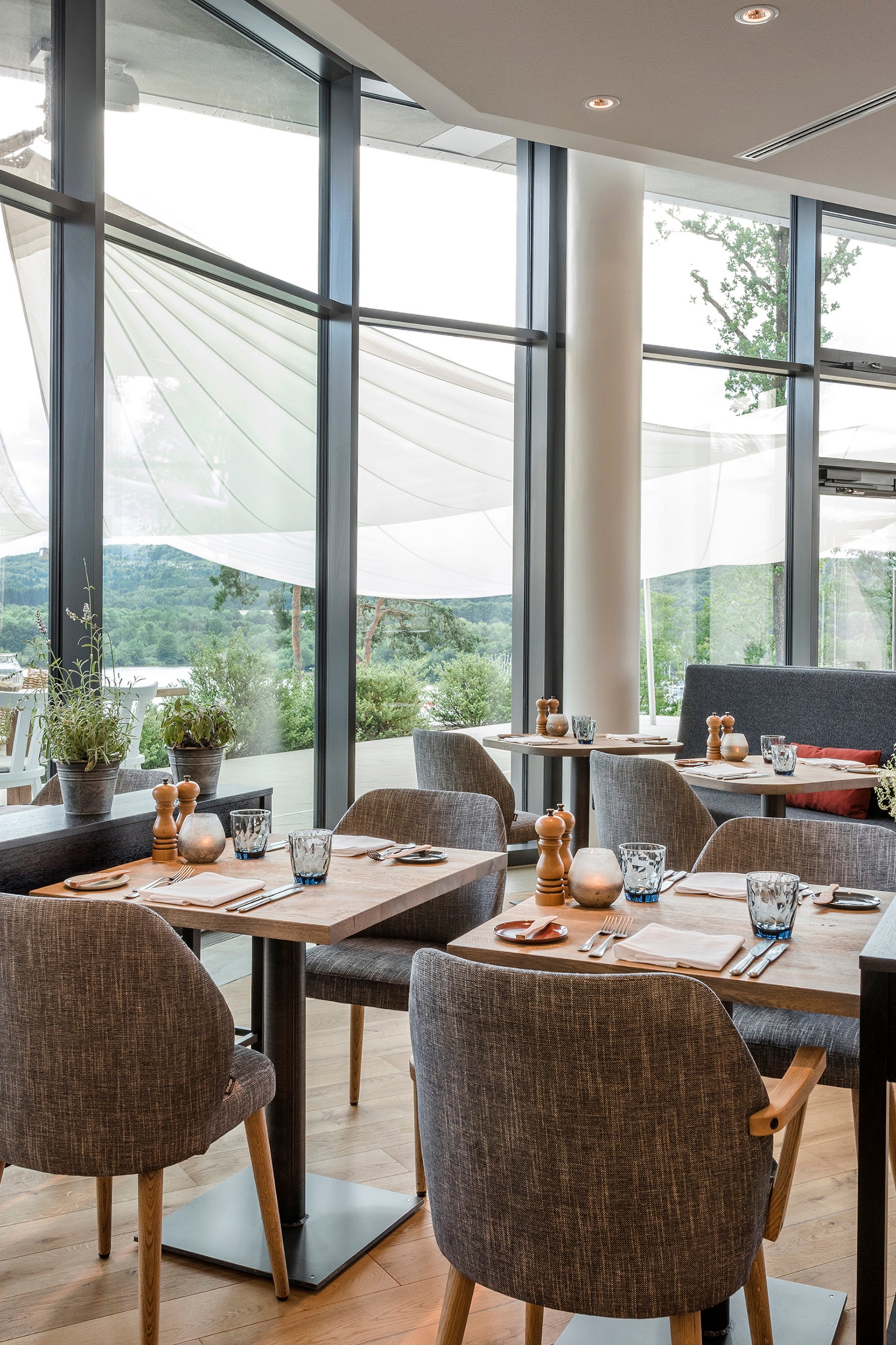 Salle de restaurant moderne avec parquet, tables et chaises, grandes fenêtres et vue