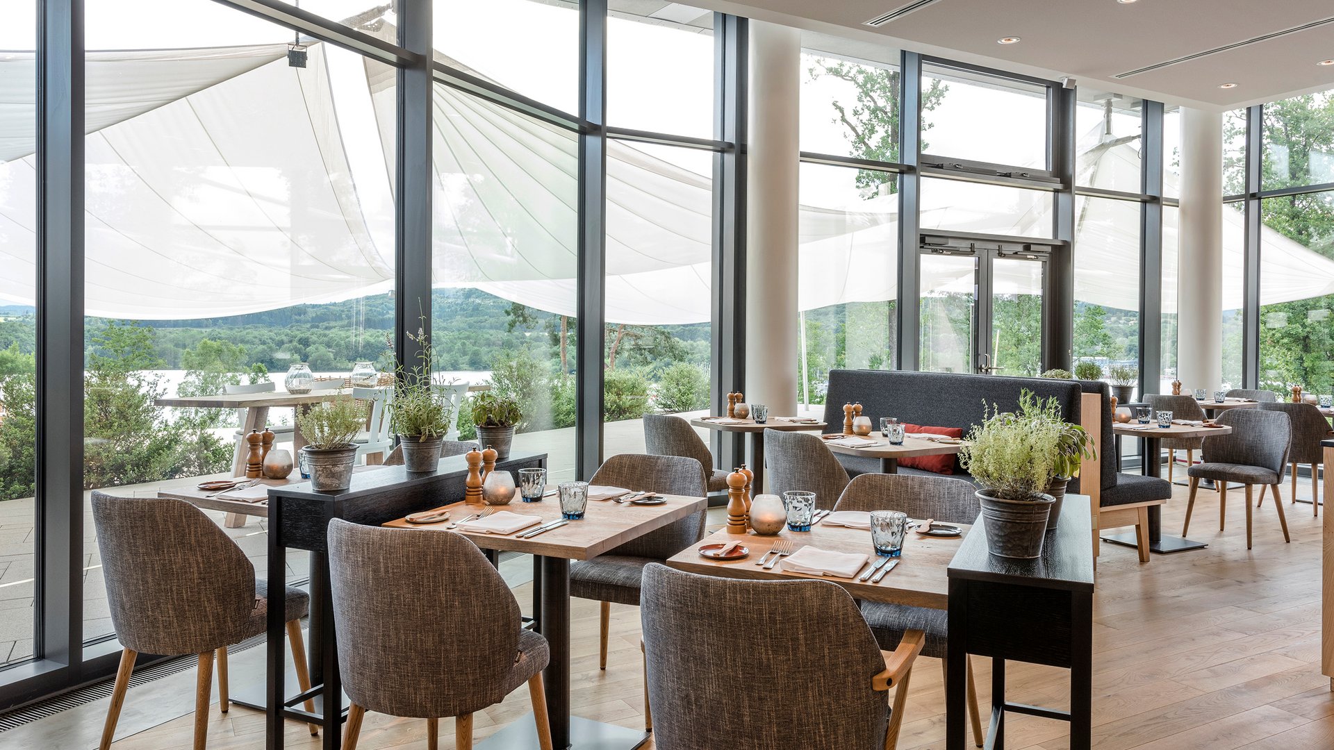 Salle de restaurant moderne avec parquet, tables et chaises, grandes fenêtres et vue