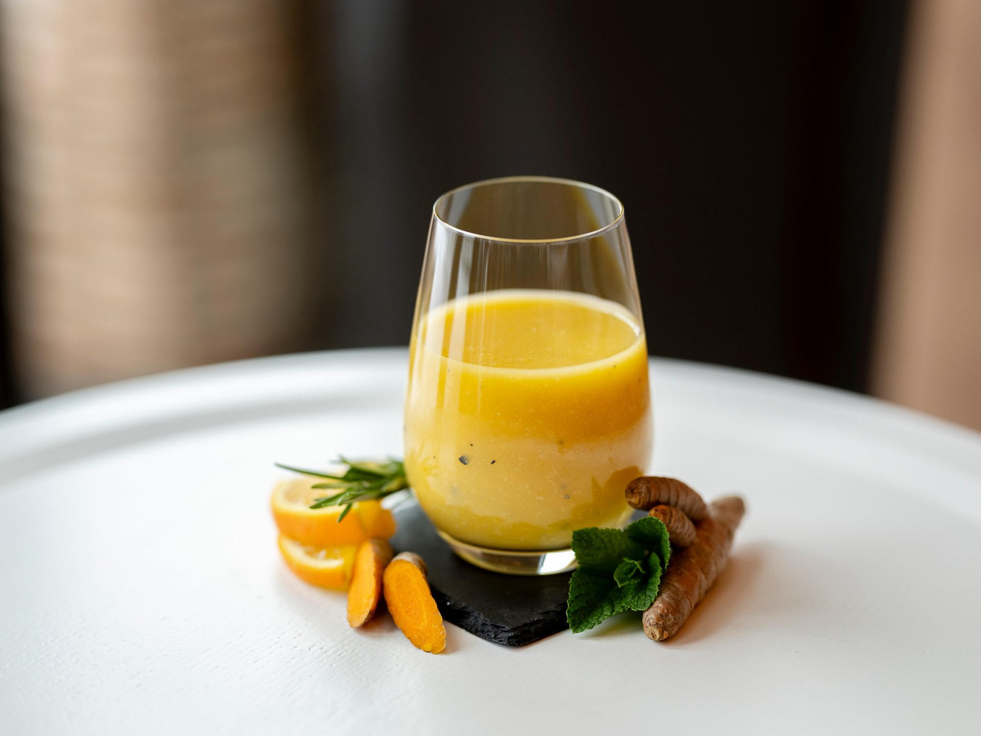 Gelber Kurkuma-Saft in Glas mit frischen Kurkumastücken und Zitronenscheiben