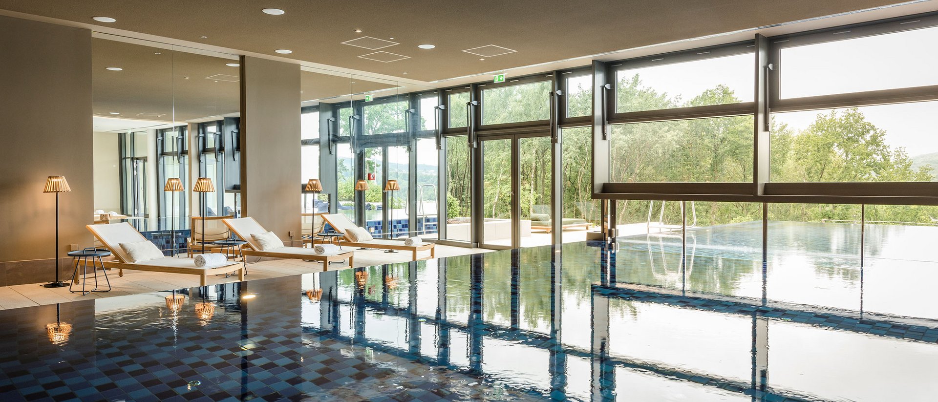 Piscine intérieure avec chaises longues et grandes fenêtres donnant sur la nature