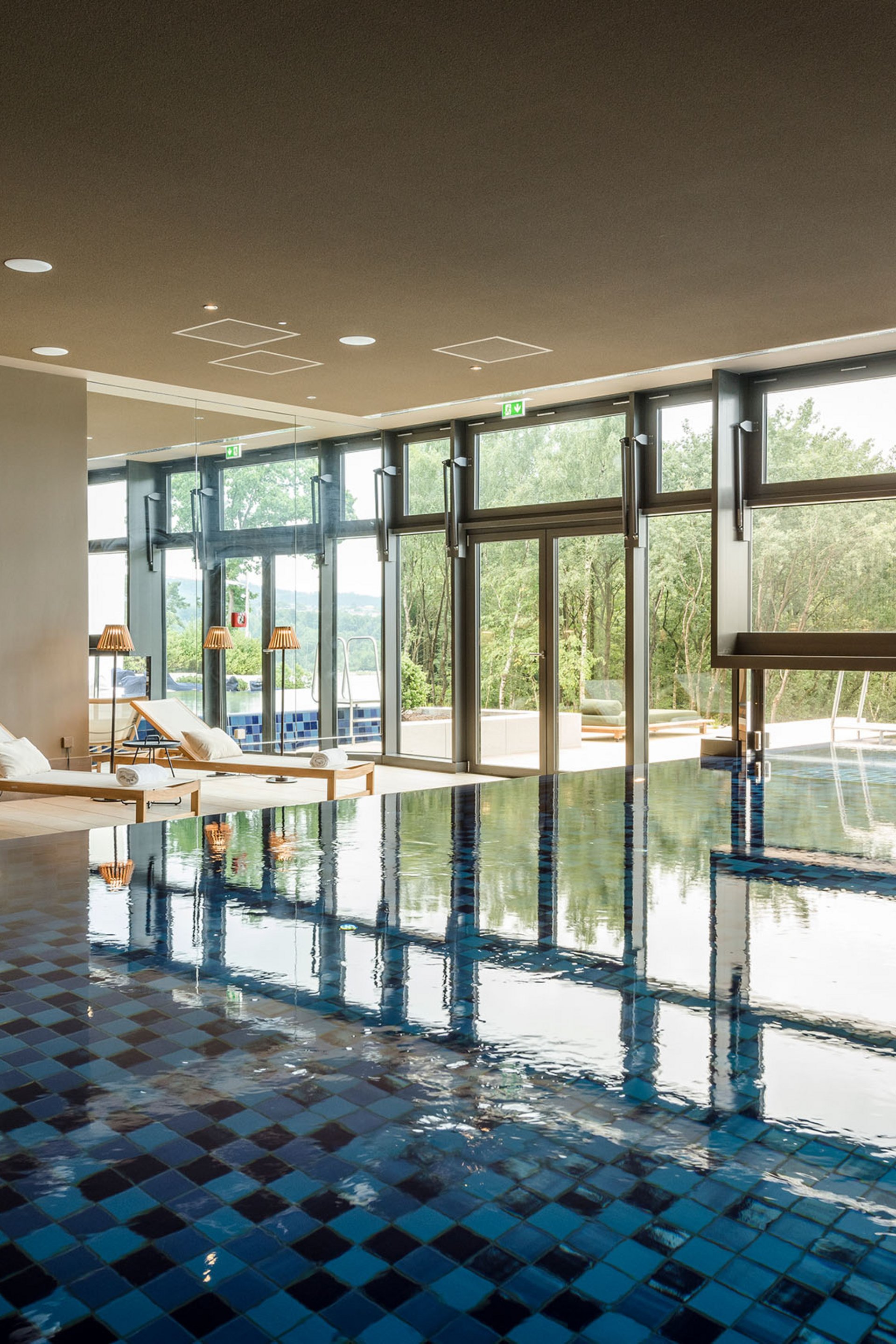 Innenpool mit Liegestühlen und großem Fenster mit Blick ins Grüne
