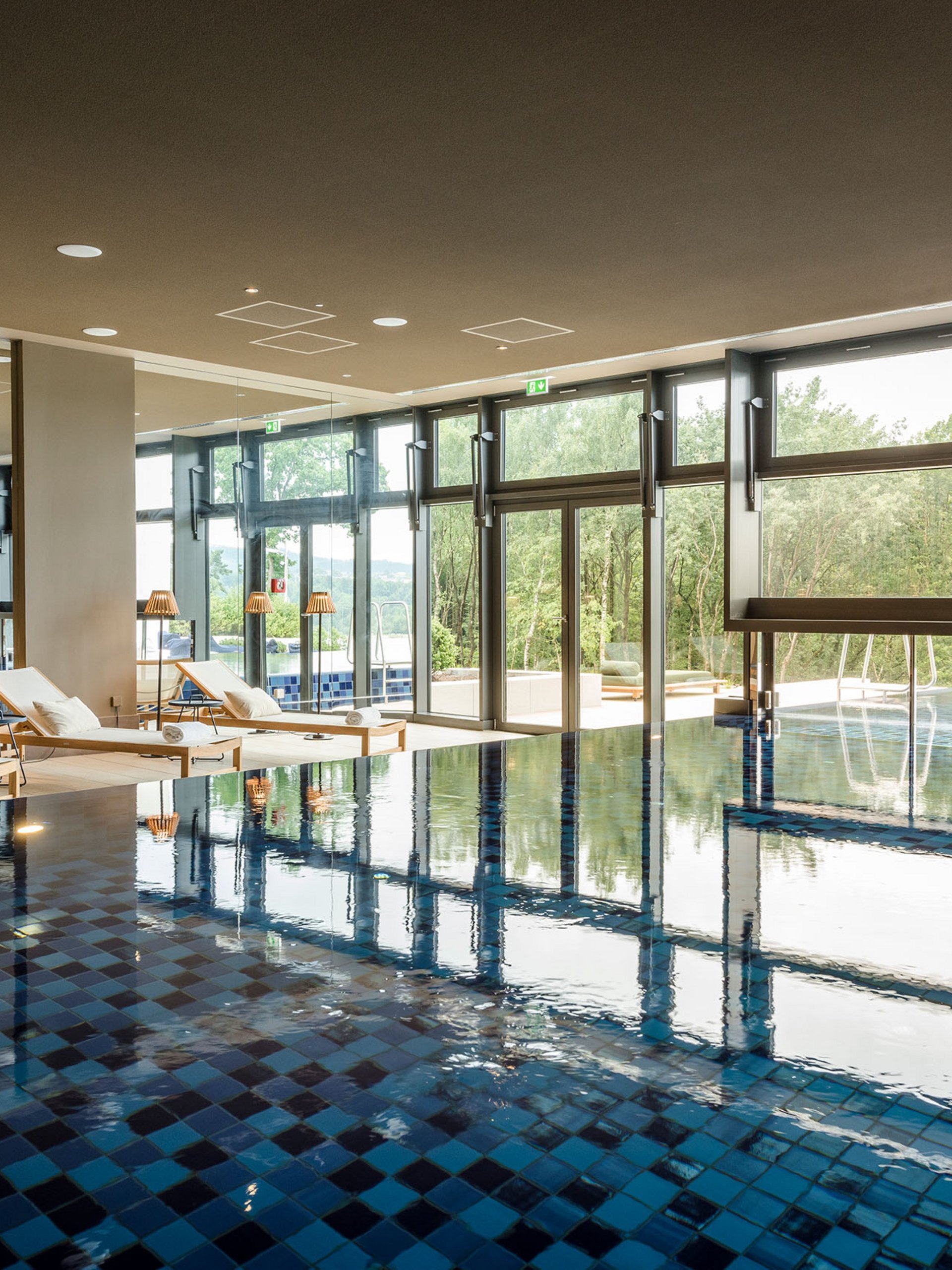 Innenpool mit Liegestühlen und großem Fenster mit Blick ins Grüne