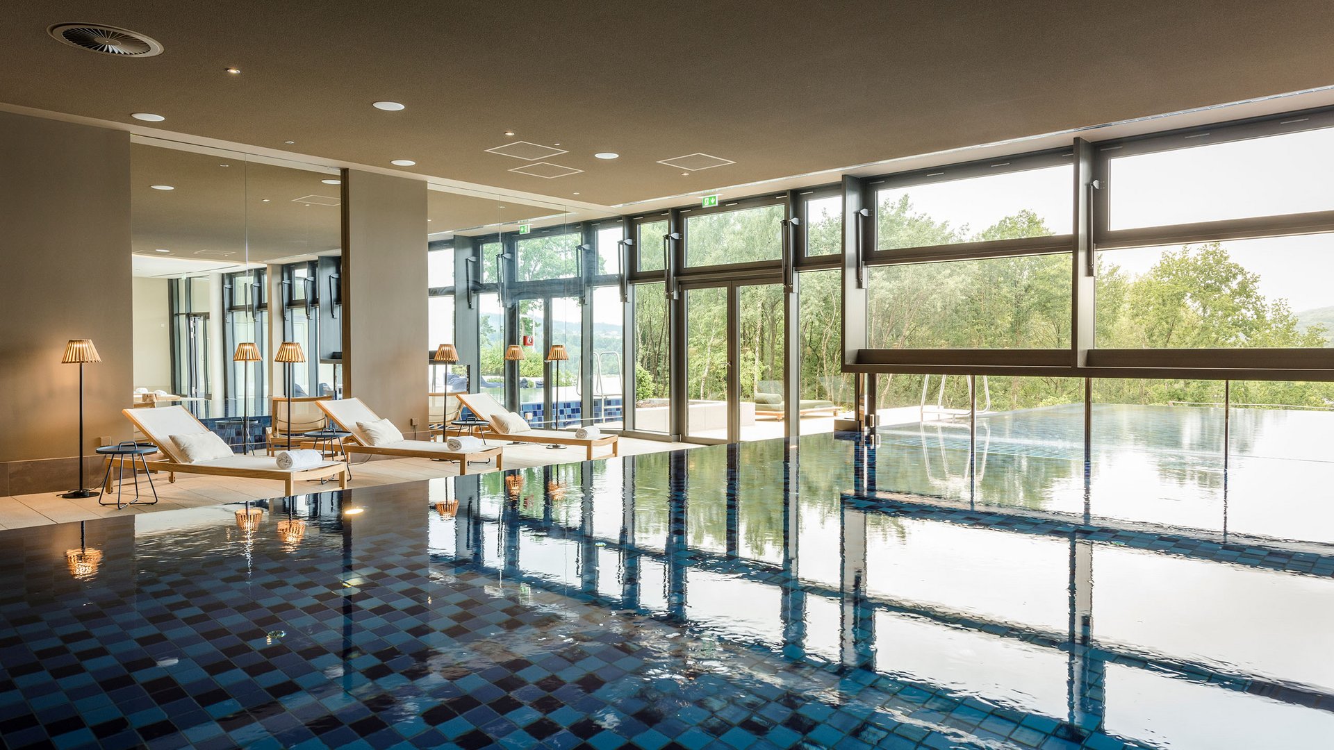 Indoor pool with lounge chairs and large windows overlooking greenery