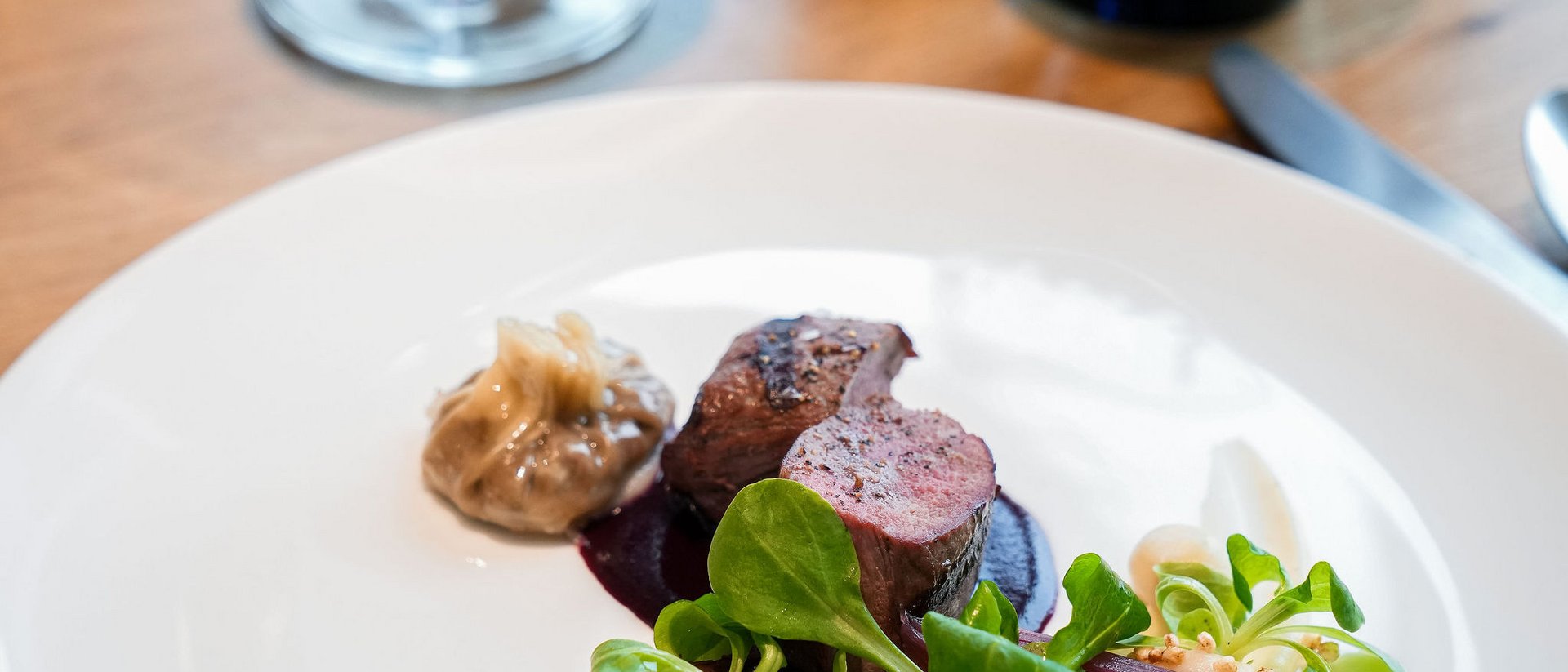 Elegant dish with meat, sauce, green salad, and red wine in the background