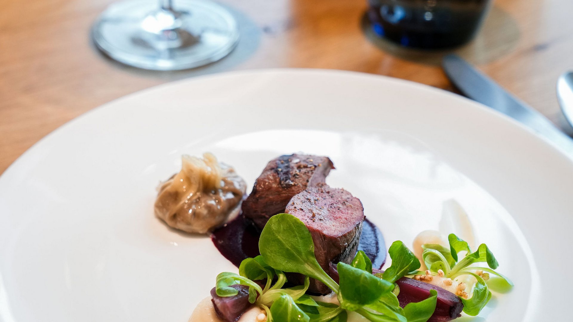 Elegantes Gericht mit Fleisch, Sauce, grünem Salat und Rotwein im Hintergrund