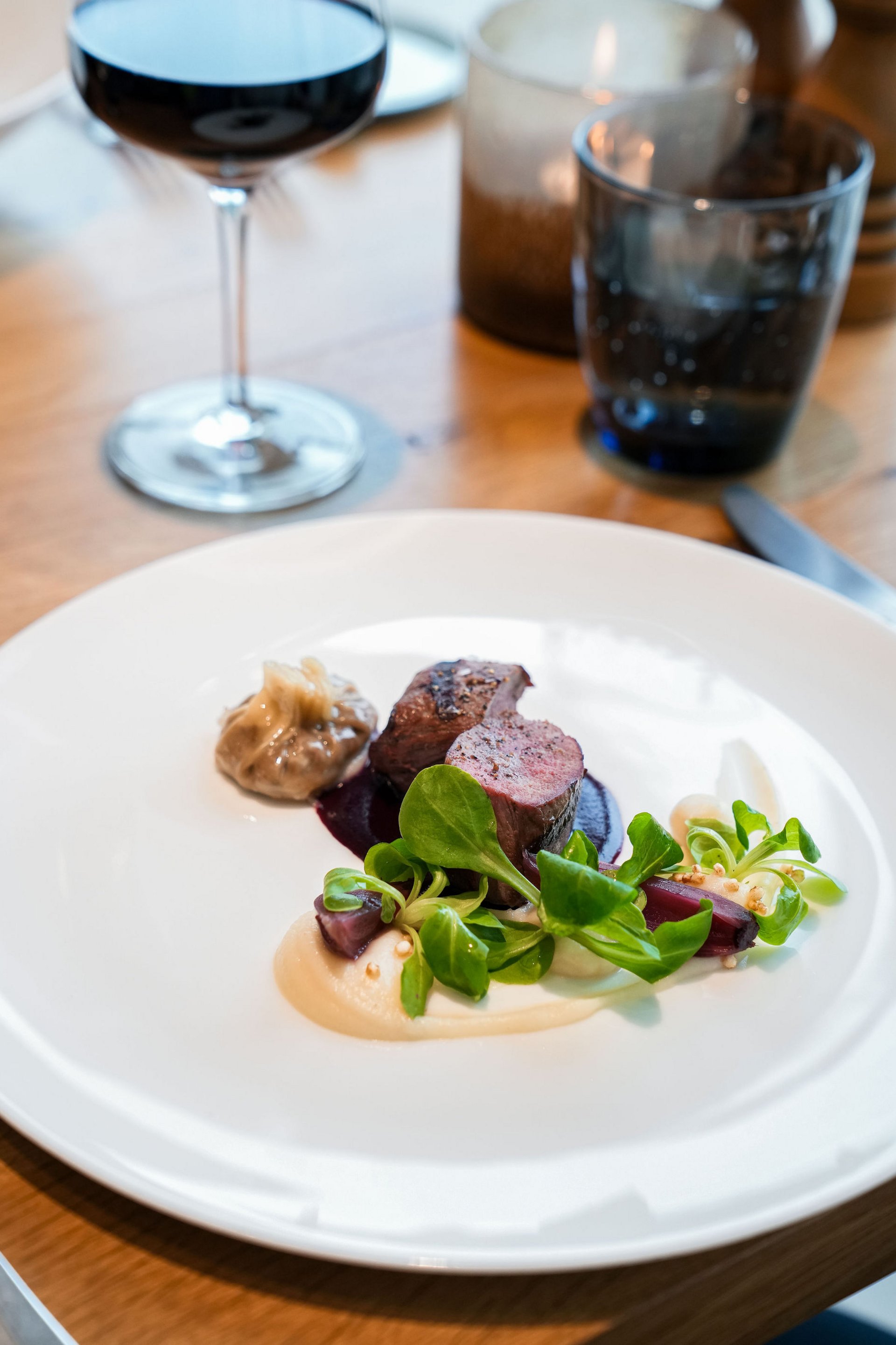 Elegantes Gericht mit Fleisch, Sauce, grünem Salat und Rotwein im Hintergrund