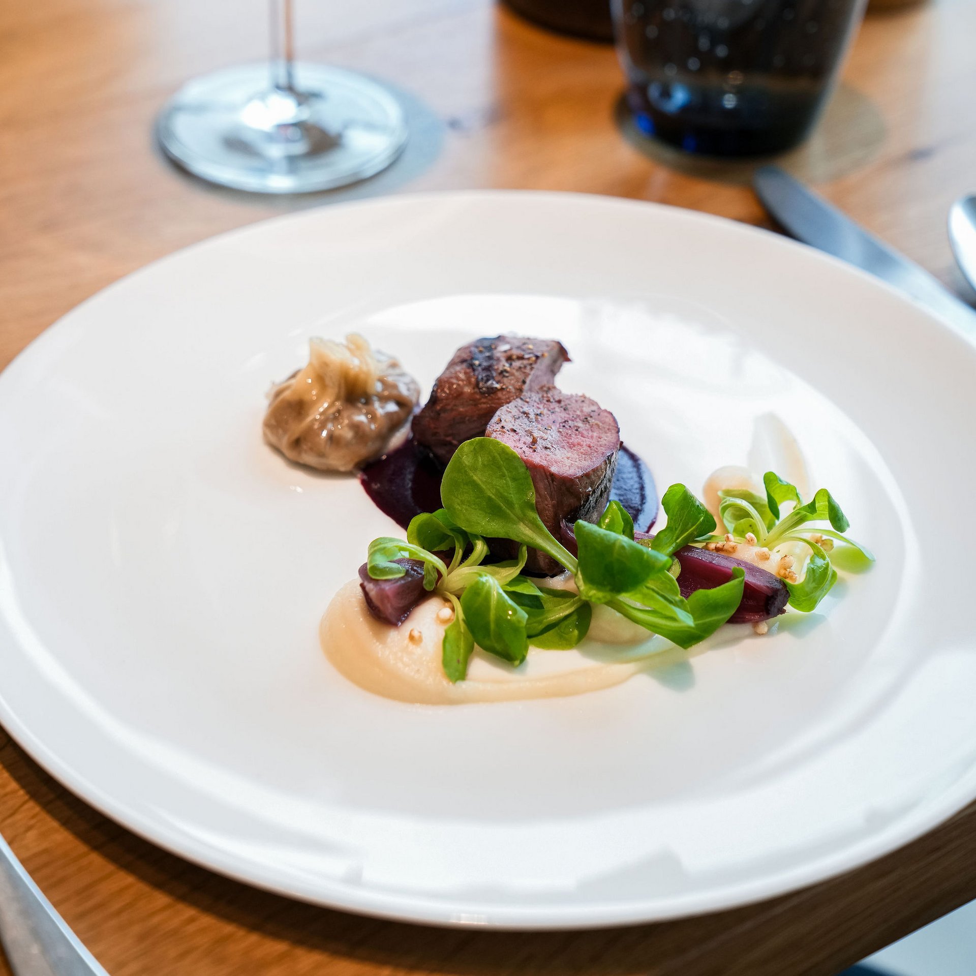 Plat raffiné avec viande, sauce, salade verte et verre de vin rouge en arrière-plan