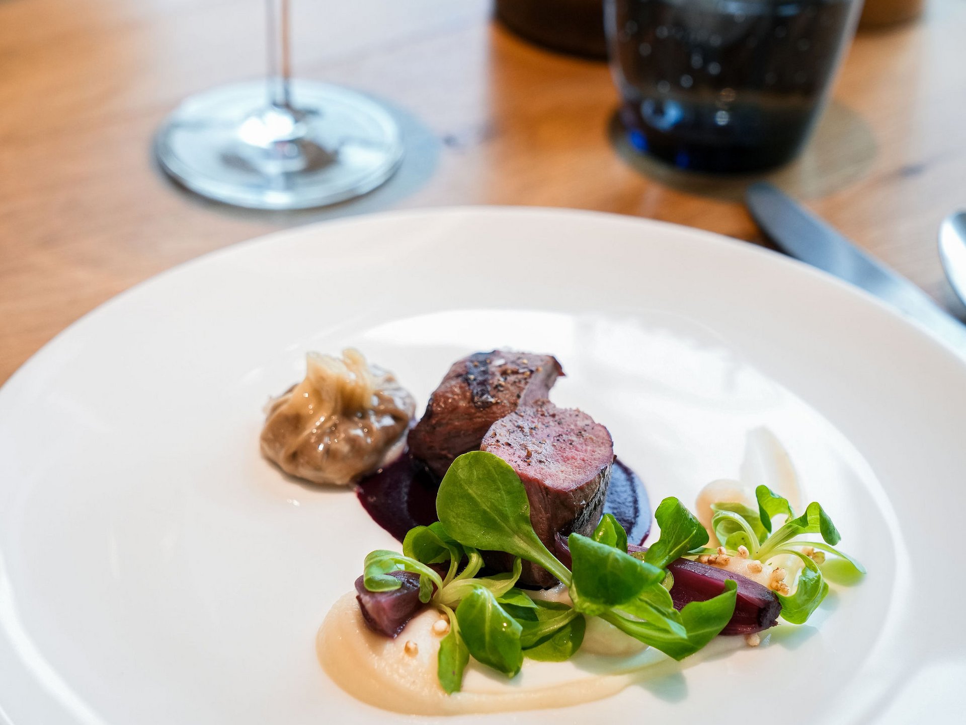 Elegant dish with meat, sauce, green salad, and red wine in the background