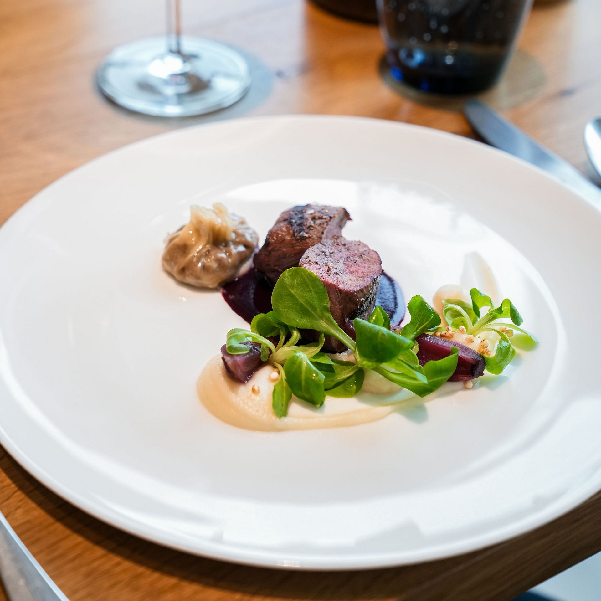 Elegantes Gericht mit Fleisch, Sauce, grünem Salat und Rotwein im Hintergrund