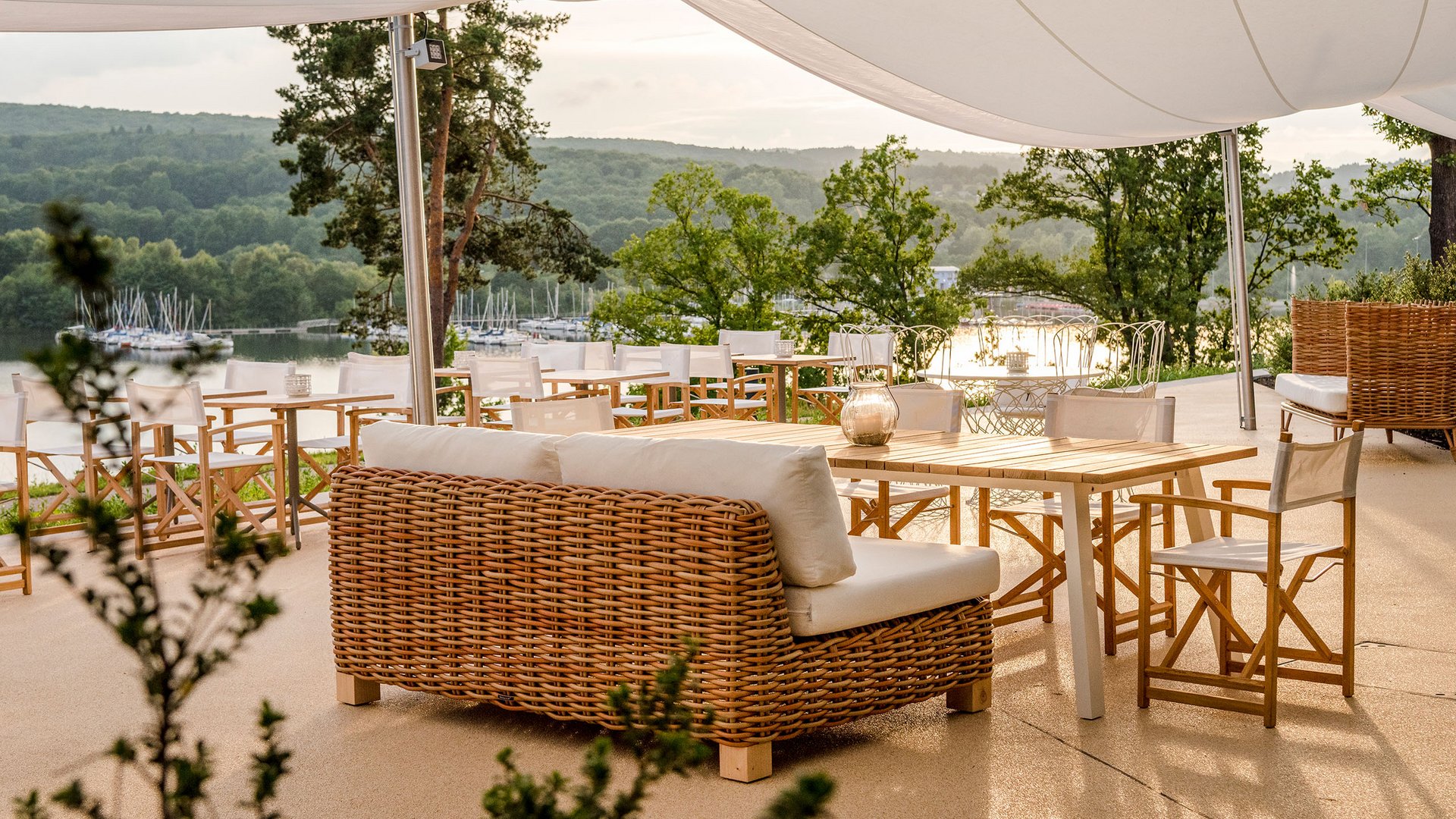 Terrasse mit Rattanmöbeln und Blick auf einen See und grüne Hügel