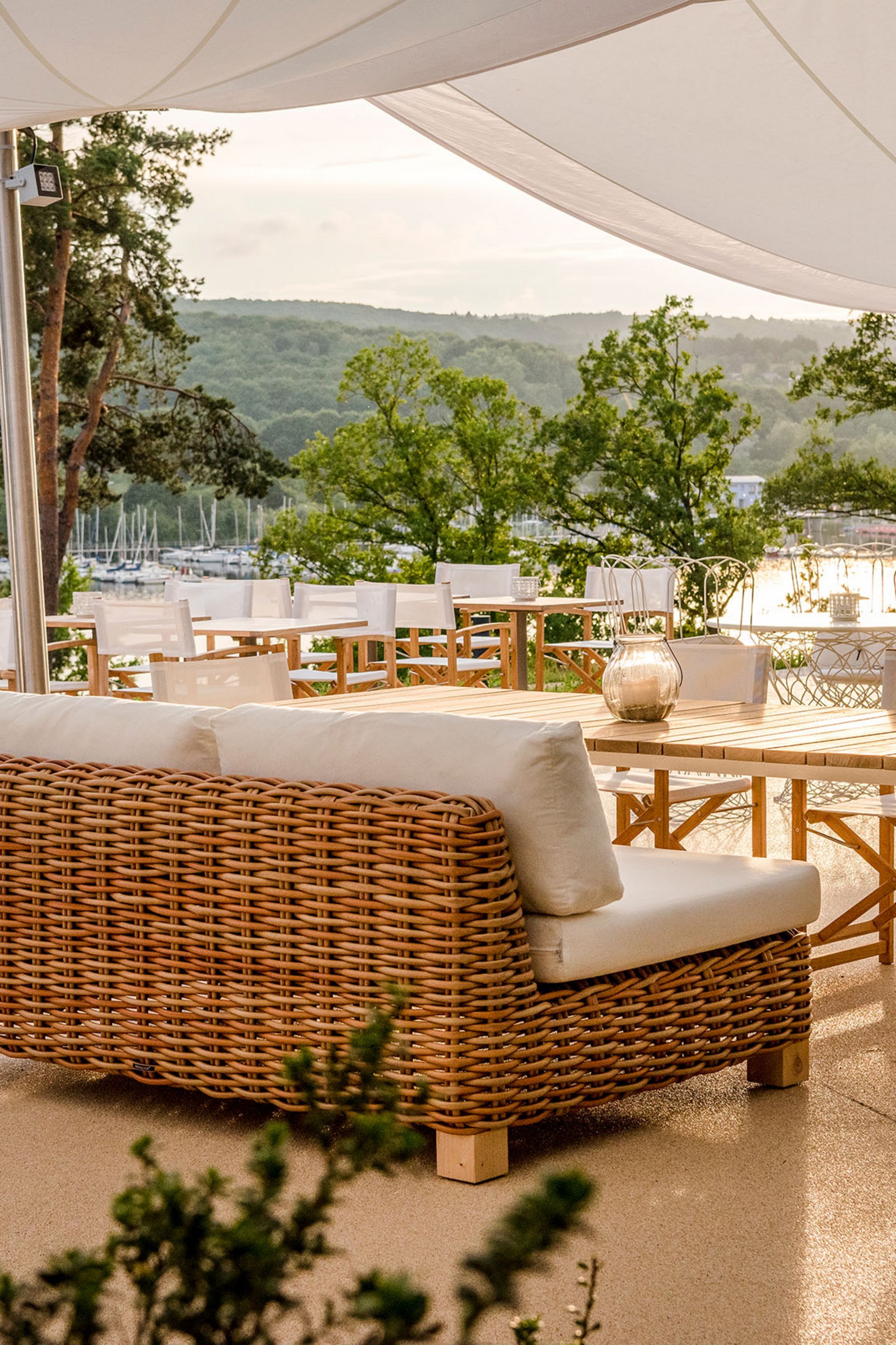 Terrasse mit Rattanmöbeln und Blick auf einen See und grüne Hügel