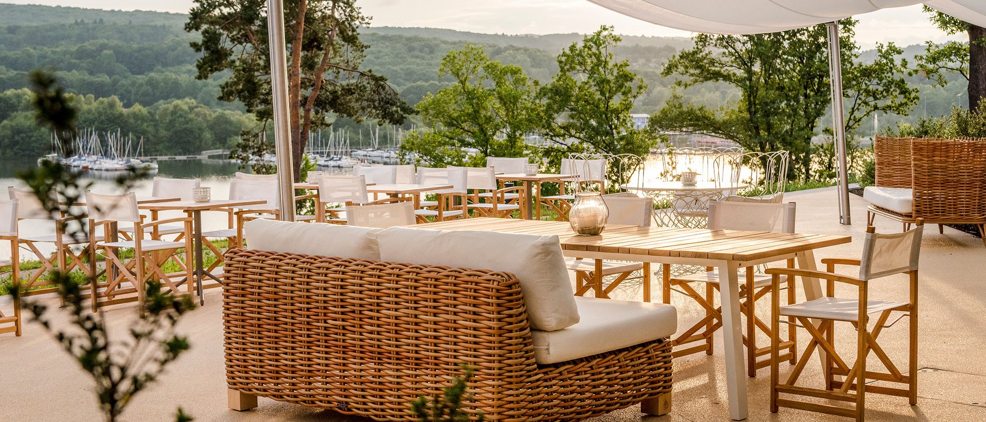 Terrasse mit Rattanmöbeln und Blick auf einen See und grüne Hügel