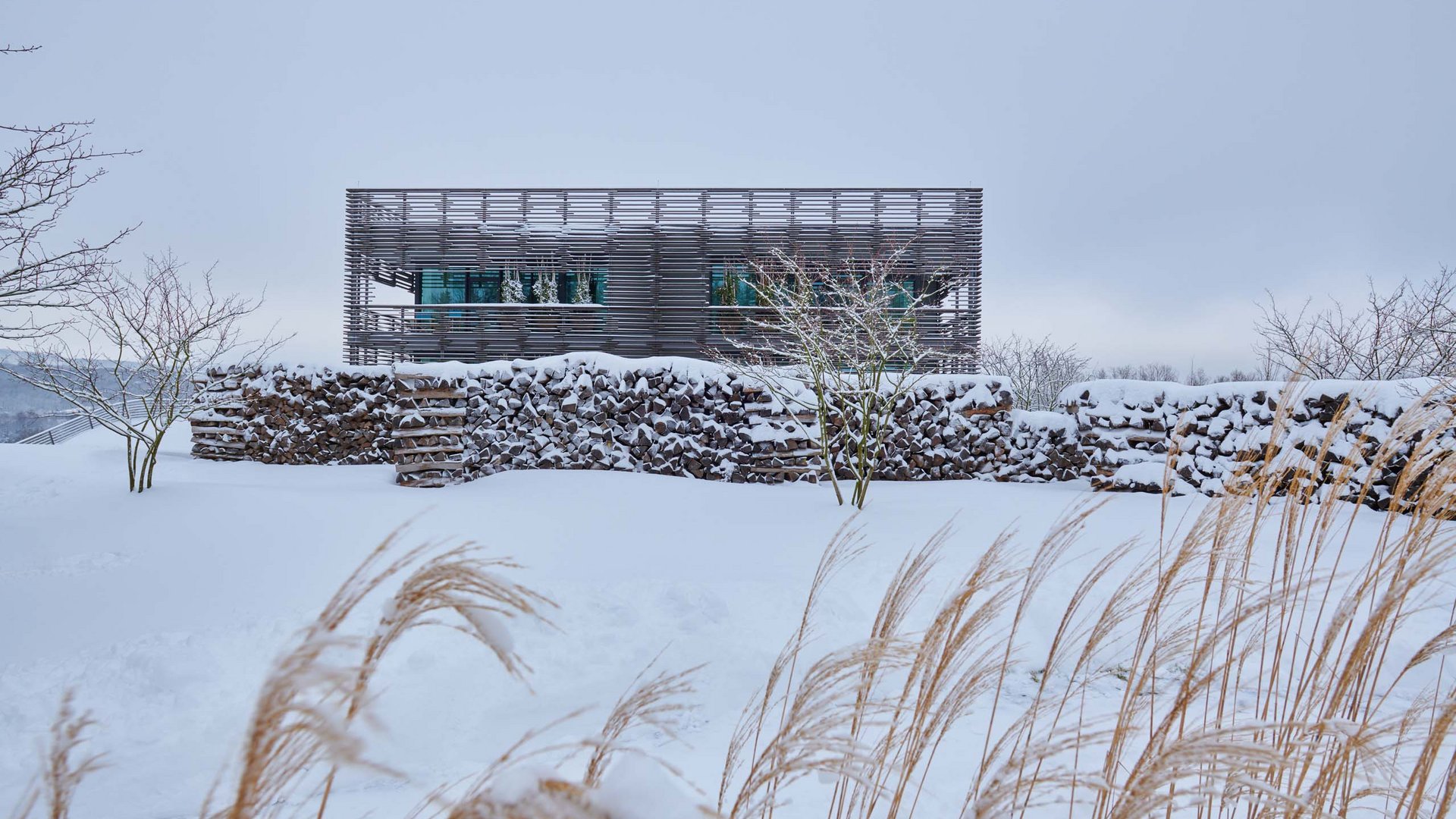 Modernes Gebäude hinter einer schneebedeckten Steinmauer in winterlicher Landschaft