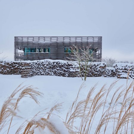 Modernes Gebäude hinter einer schneebedeckten Steinmauer in winterlicher Landschaft