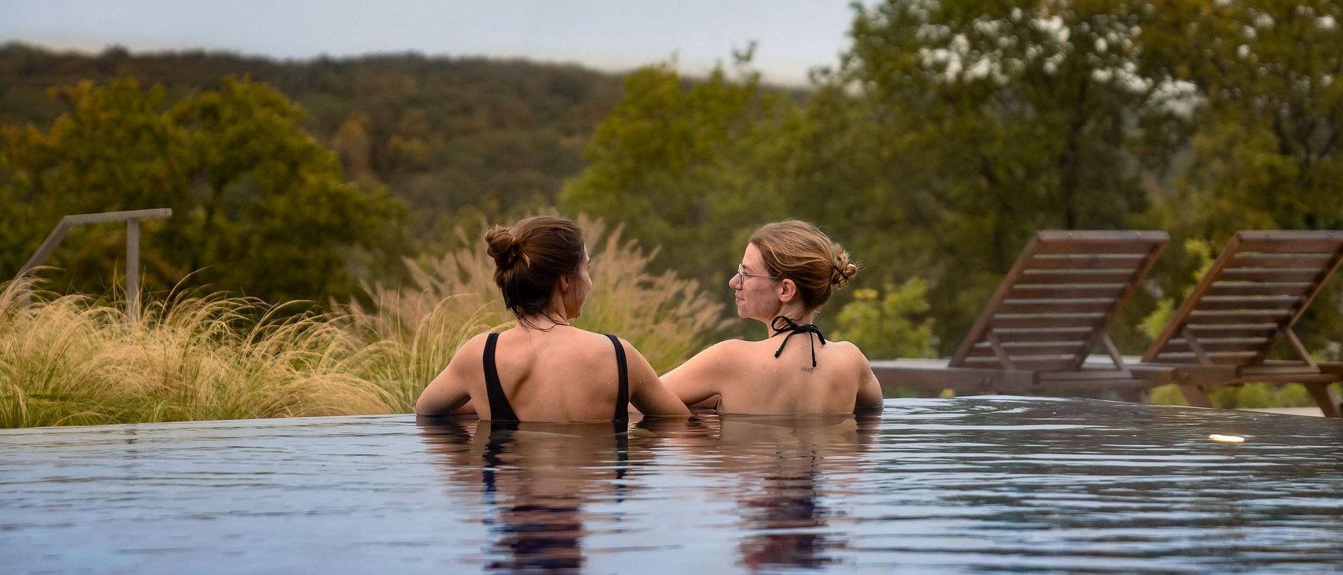 Zwei Frauen im Pool mit Blick auf grüne Landschaft und Liegestühle