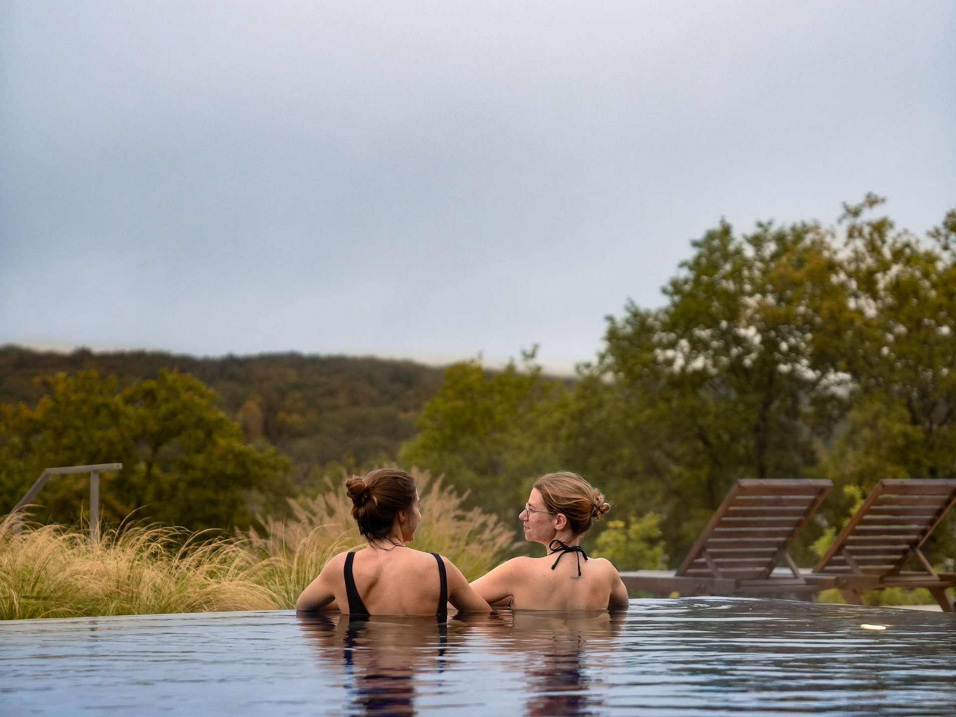Zwei Frauen im Pool mit Blick auf grüne Landschaft und Liegestühle