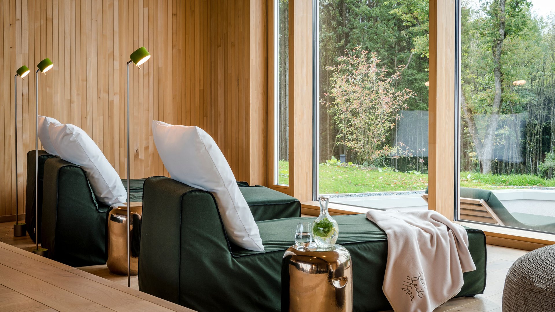 Entspannungsbereich mit Liegestuhl, Kissen, Decke und grünem Ausblick