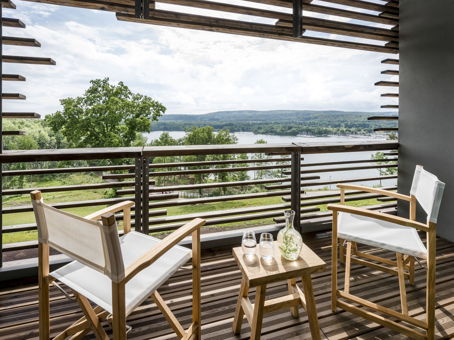Balcony with two chairs and table overlooking a lake and wooded hills