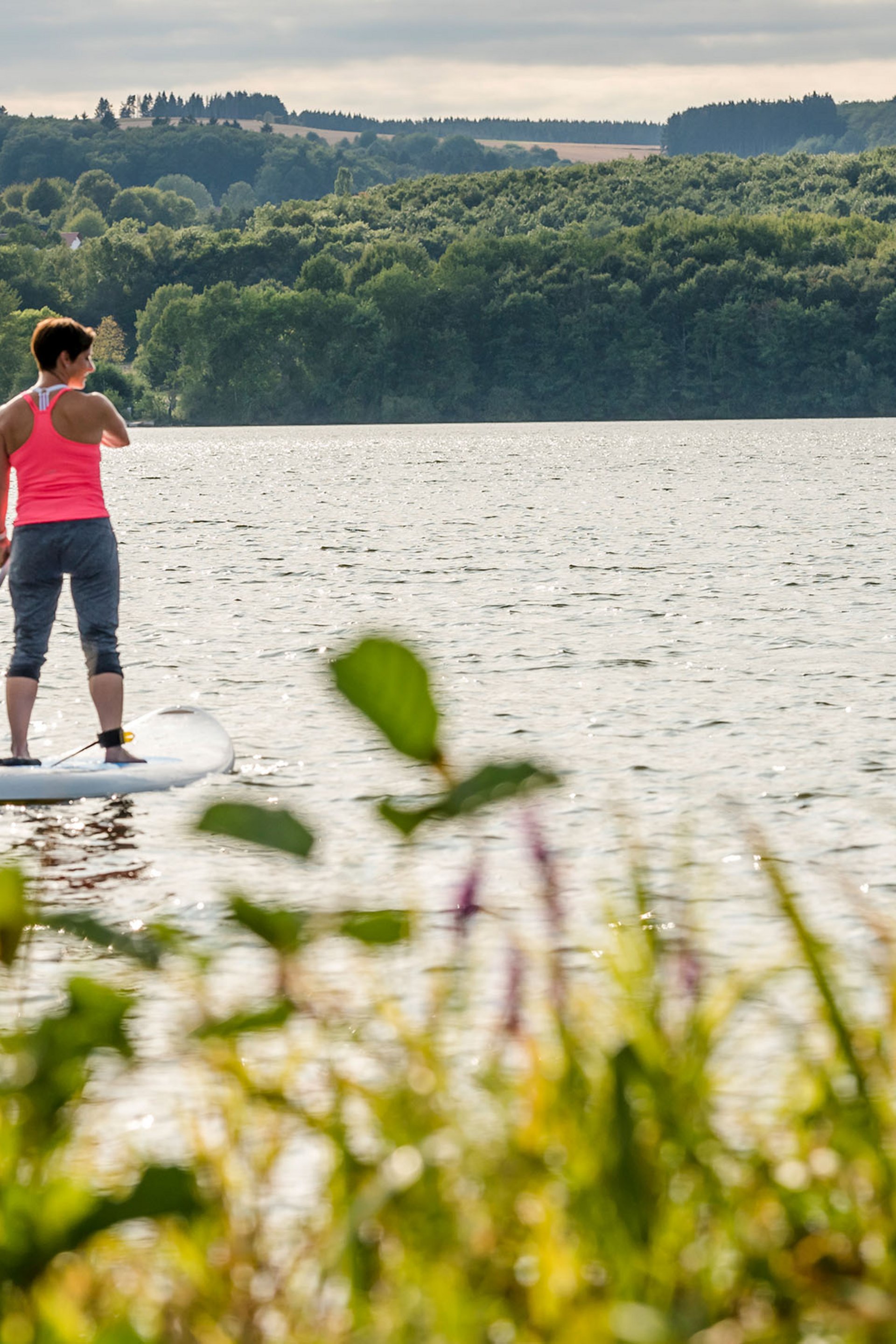 Zwei Frauen beim Stand-up-Paddling auf einem See umgeben von Wald