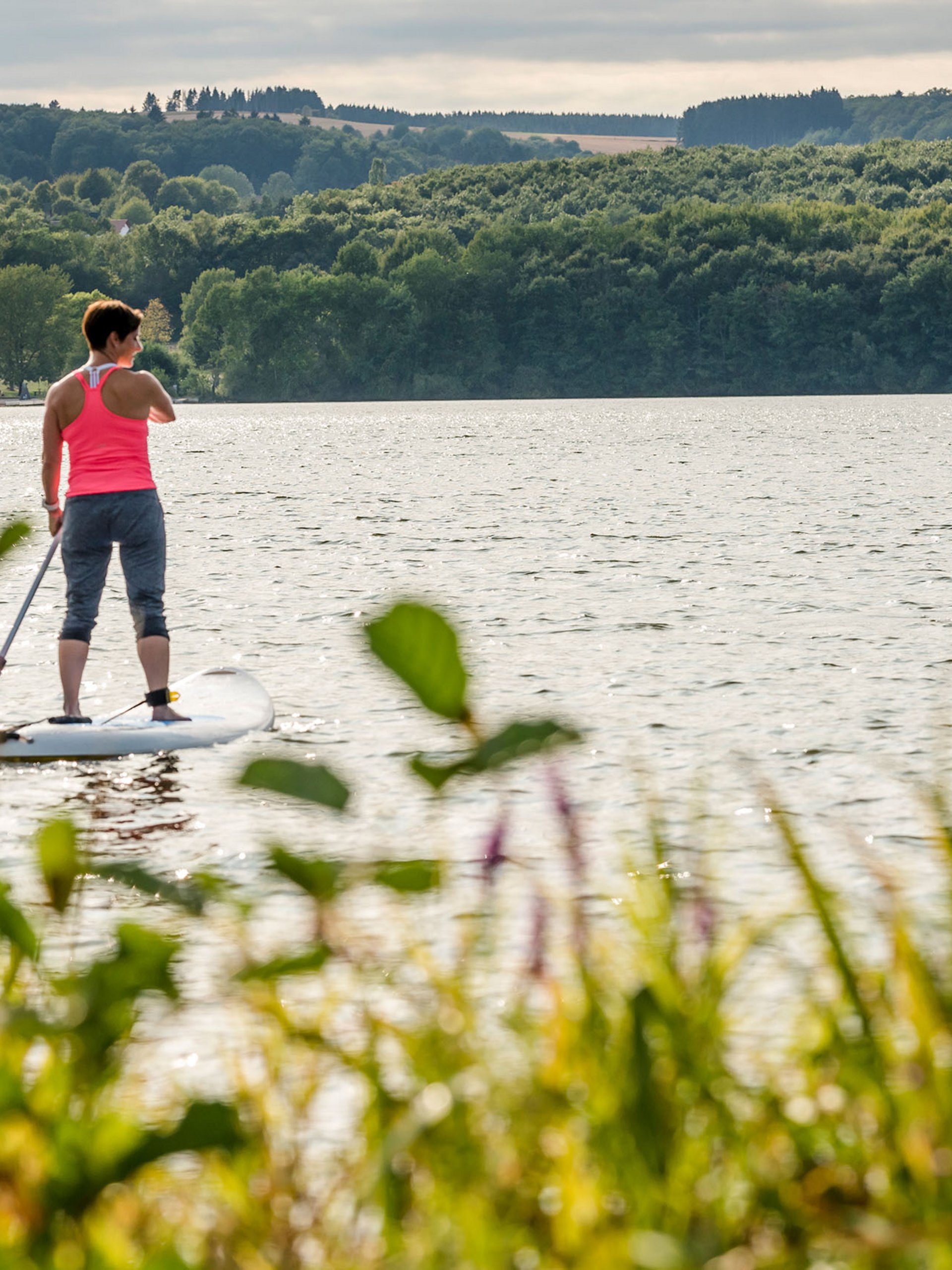 Zwei Frauen beim Stand-up-Paddling auf einem See umgeben von Wald
