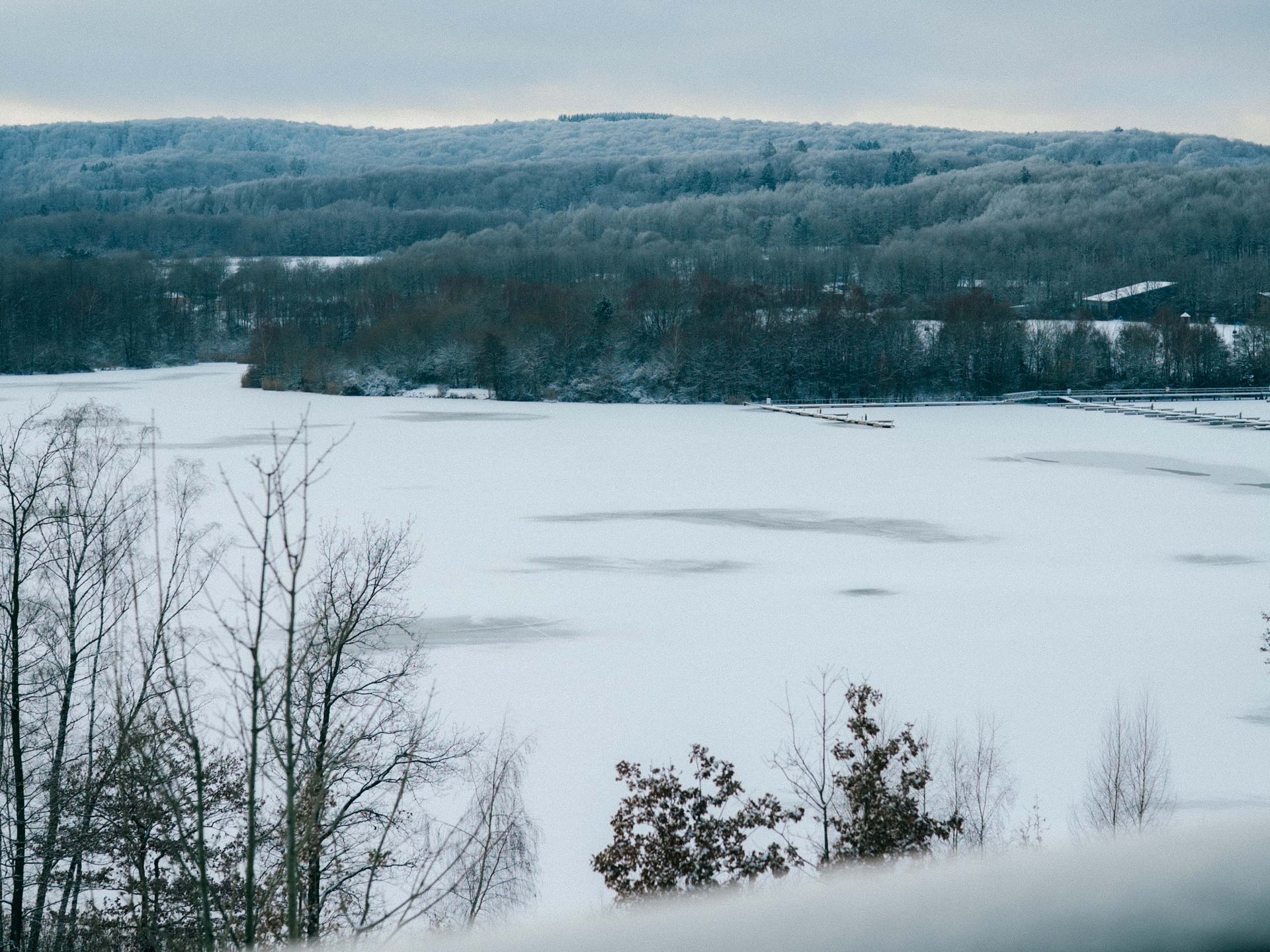 Verschneiter See vor bewaldeten Hügeln, gesehen über ein Balkongeländer