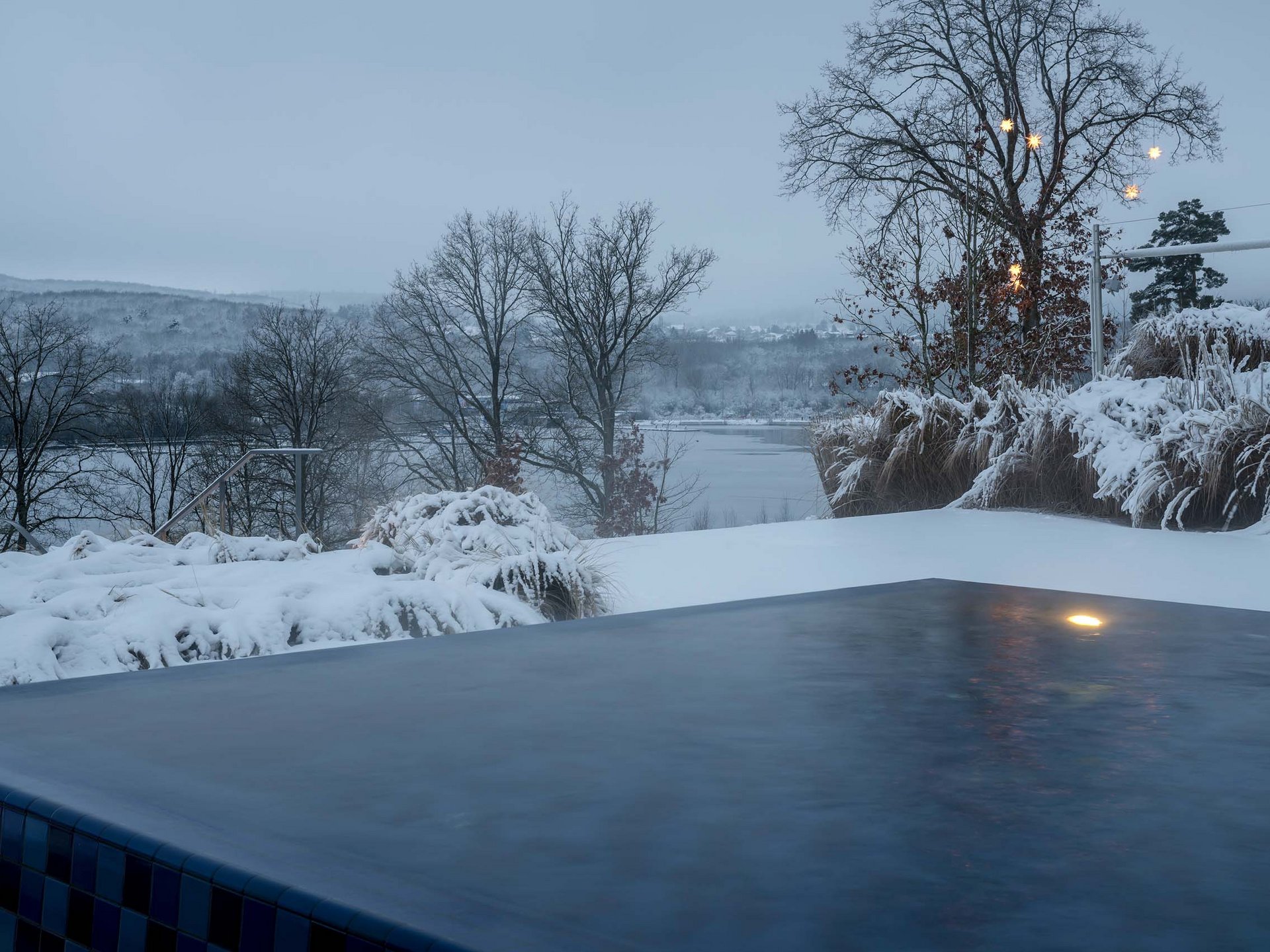 Außenpool vor einer verschneiten Winterlandschaft mit kahlen Bäumen