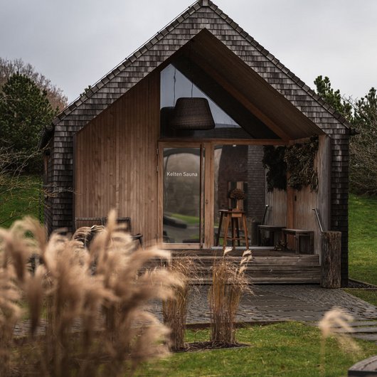 Modernes Holzhaus mit Kelten Sauna umgeben von Gras und Gehweg bei bewölktem Himmel