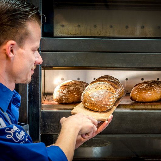 Bäcker holt frisch gebackenes Brot aus dem Ofen