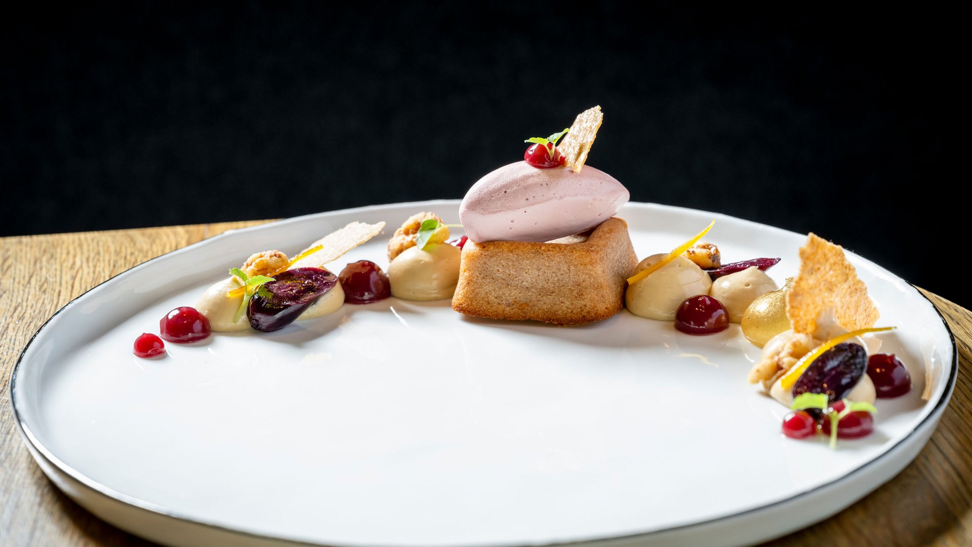 Elegantes Dessert mit Biskuit, Eis und Fruchtsoßen auf weißem Teller