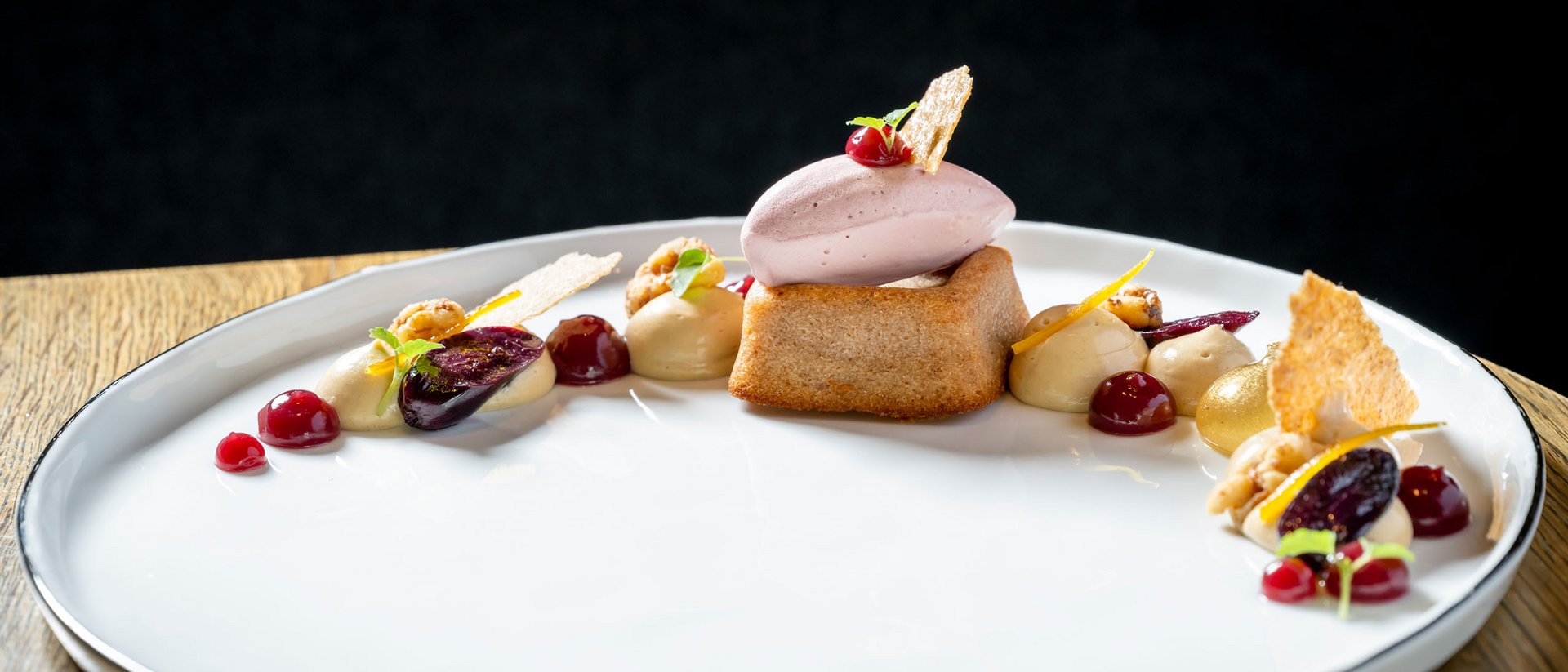 Elegantes Dessert mit Biskuit, Eis und Fruchtsoßen auf weißem Teller