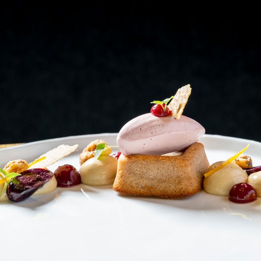 Elegantes Dessert mit Biskuit, Eis und Fruchtsoßen auf weißem Teller