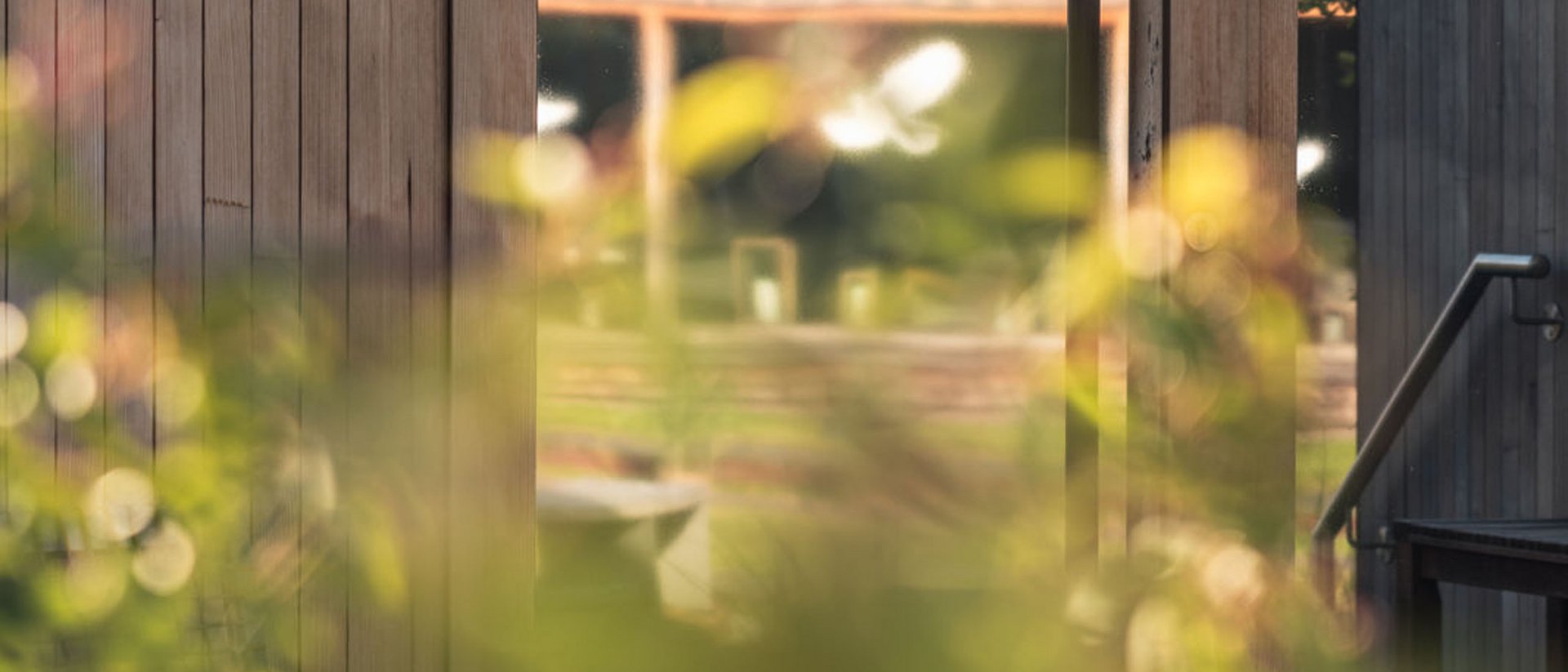 Glass door with Kelten Sauna sign and wooden wall with blurred plants in front