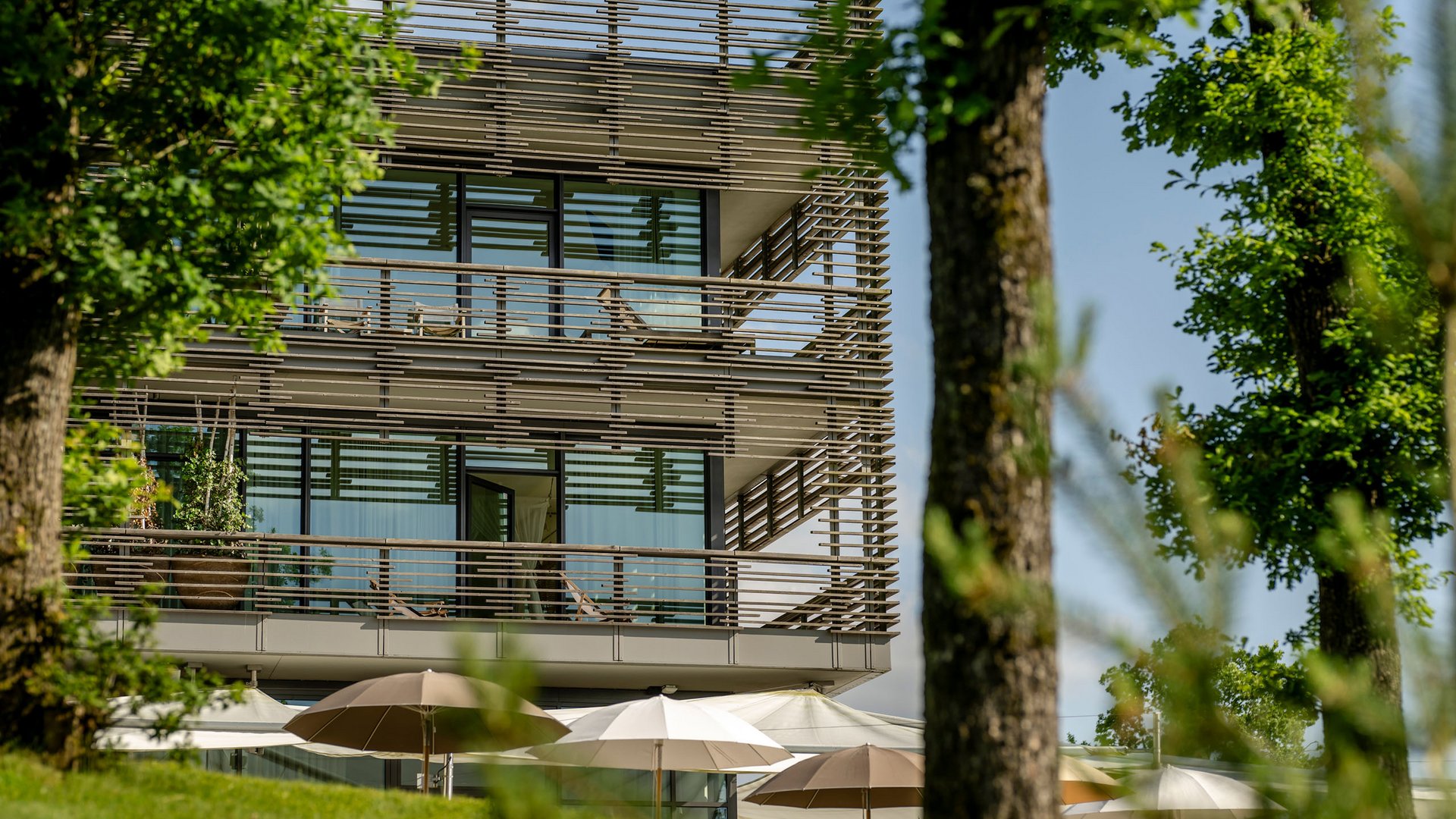Modernes Gebäude mit großen Glasfenstern und Sonnenschirmen im Garten