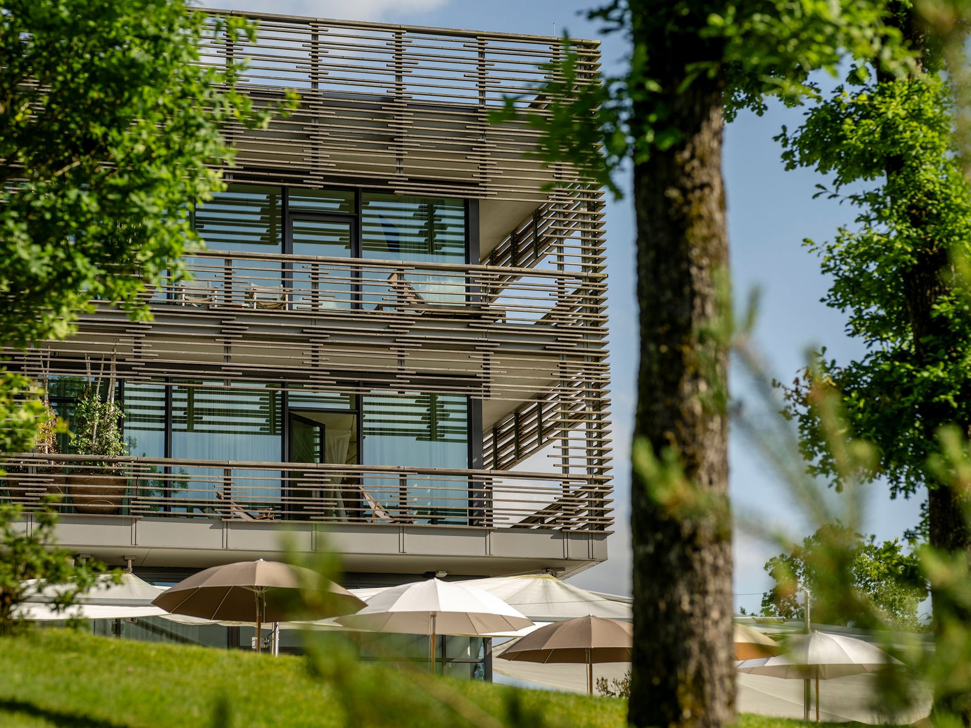 Modernes Gebäude mit großen Glasfenstern und Sonnenschirmen im Garten