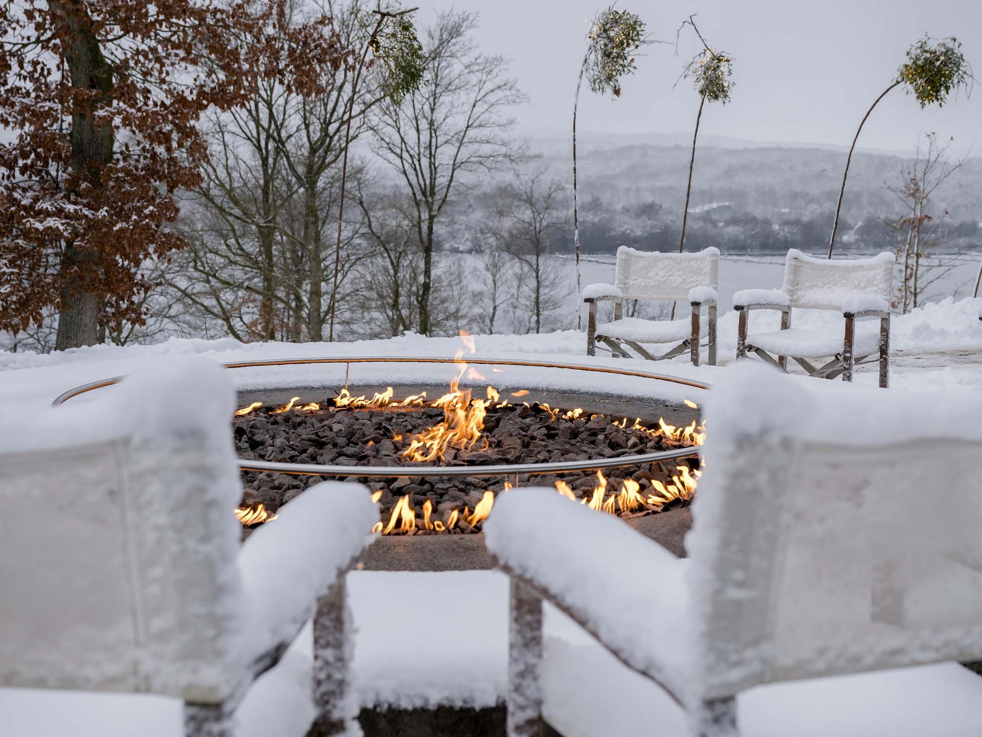 Schneebedeckte Sitzgruppe mit Feuerstelle und Blick auf eine winterliche Landschaft