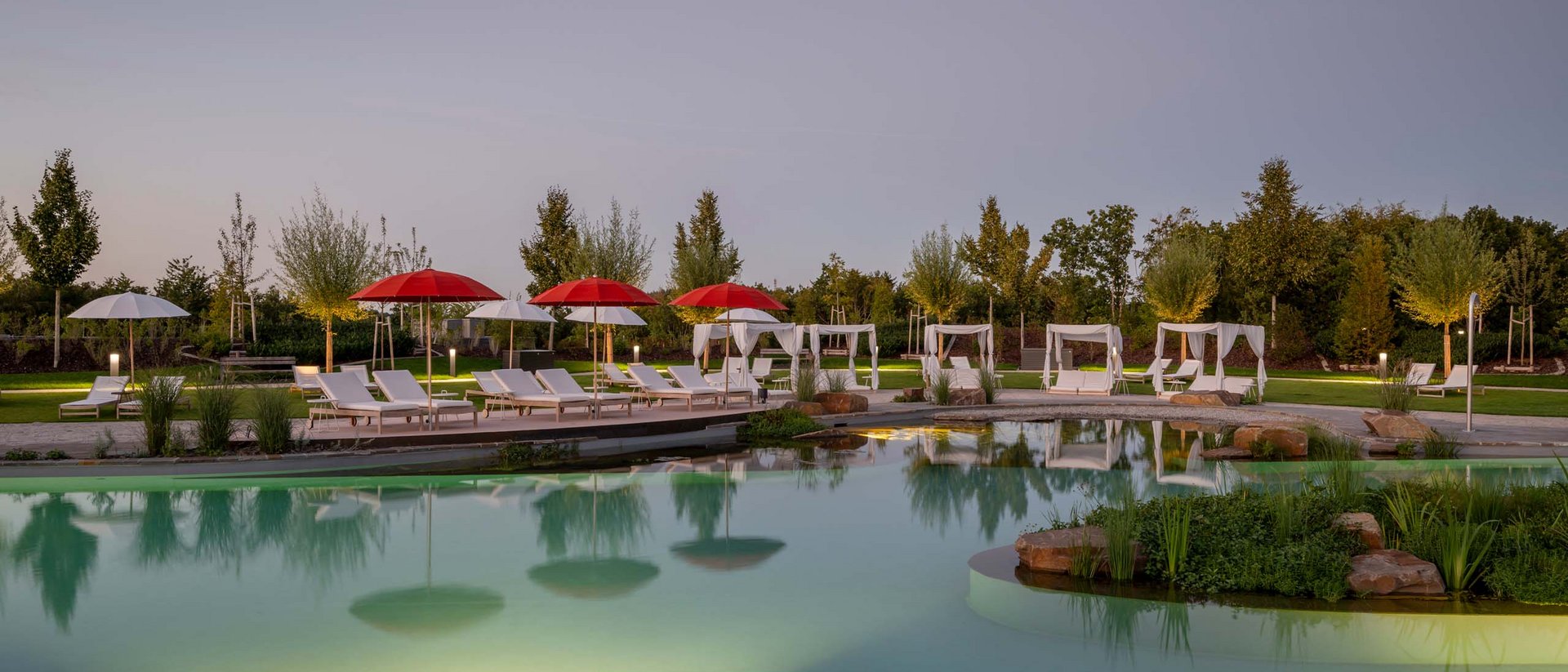 Abendblick auf einen beleuchteten Pool mit roten und weißen Sonnenschirmen und Liegestühlen