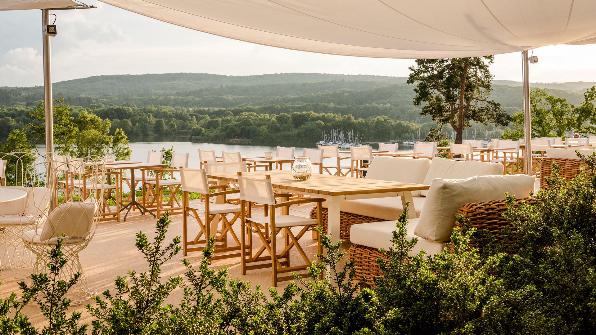 Terrasse ensoleillée avec chaises blanches et vue sur le lac sous un auvent