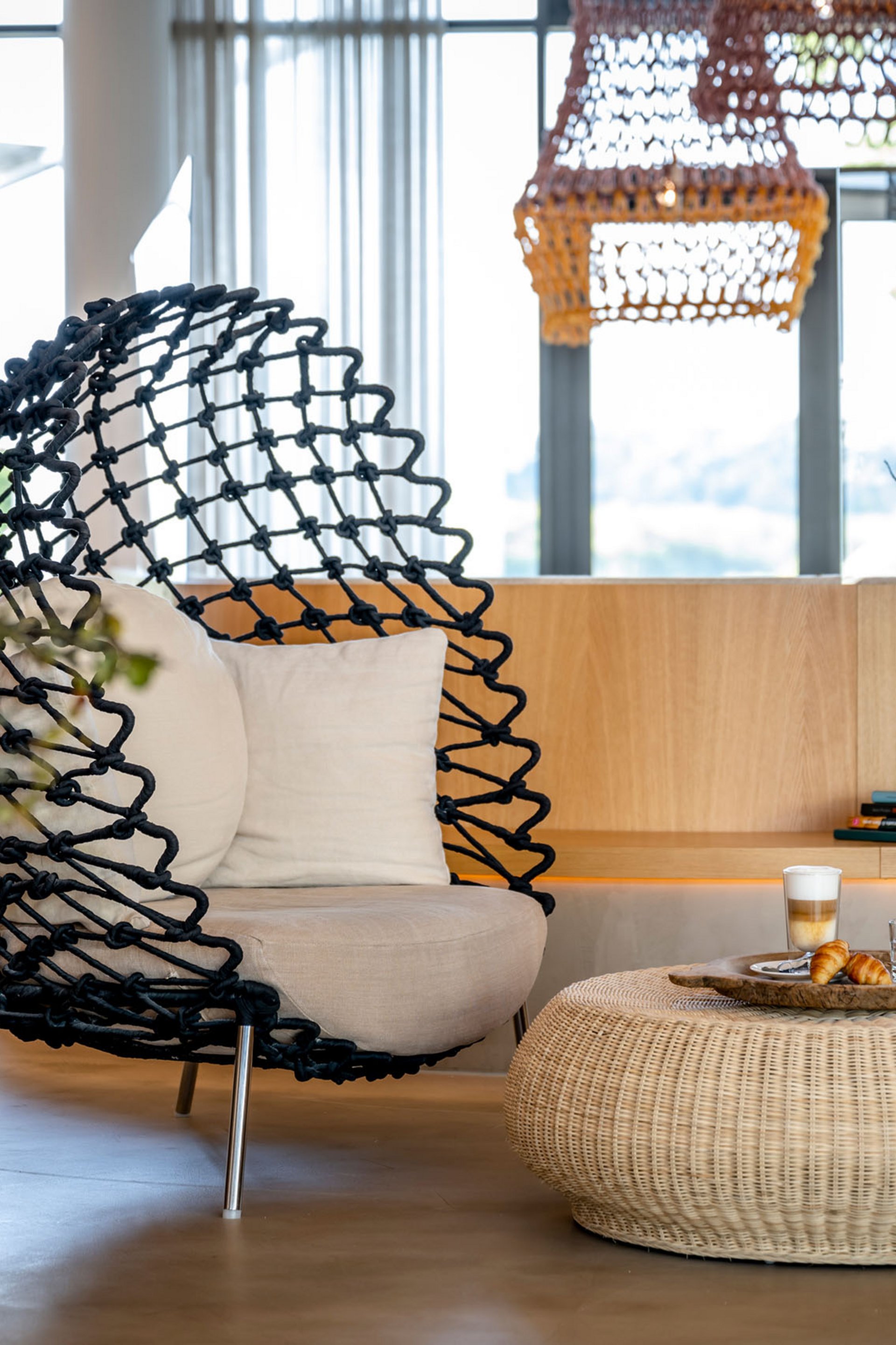 Espace salon moderne avec fauteuil noir, table en rotin et fleurs dans un salon lumineux
