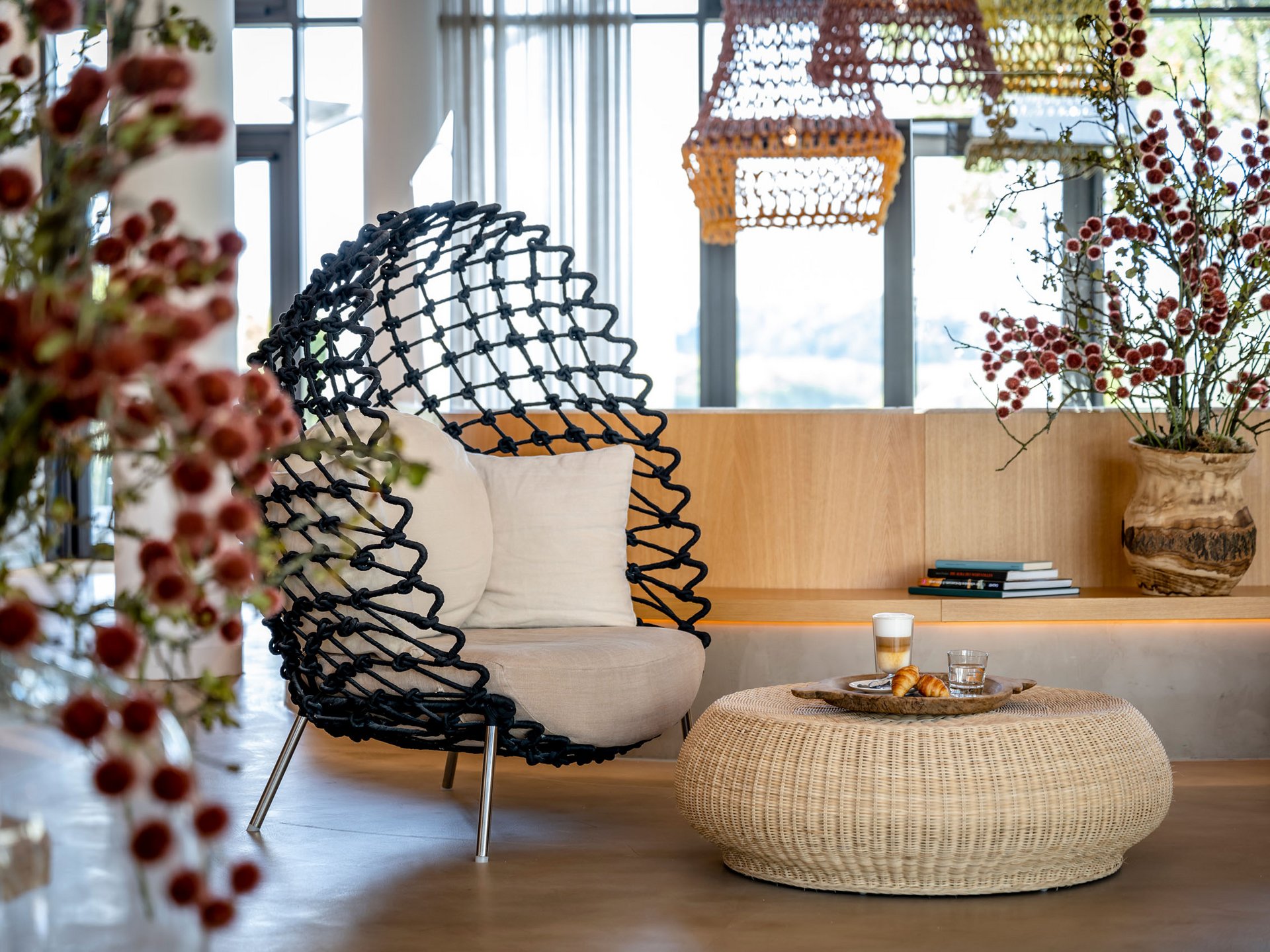 Espace salon moderne avec fauteuil noir, table en rotin et fleurs dans un salon lumineux