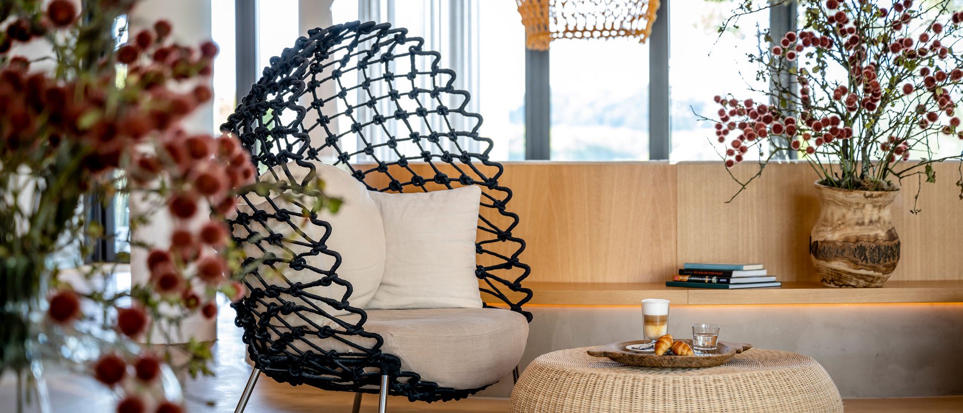 Moderner Sitzbereich mit Korbtisch, schwarzem Sessel und Blumen in einer hellen Lounge