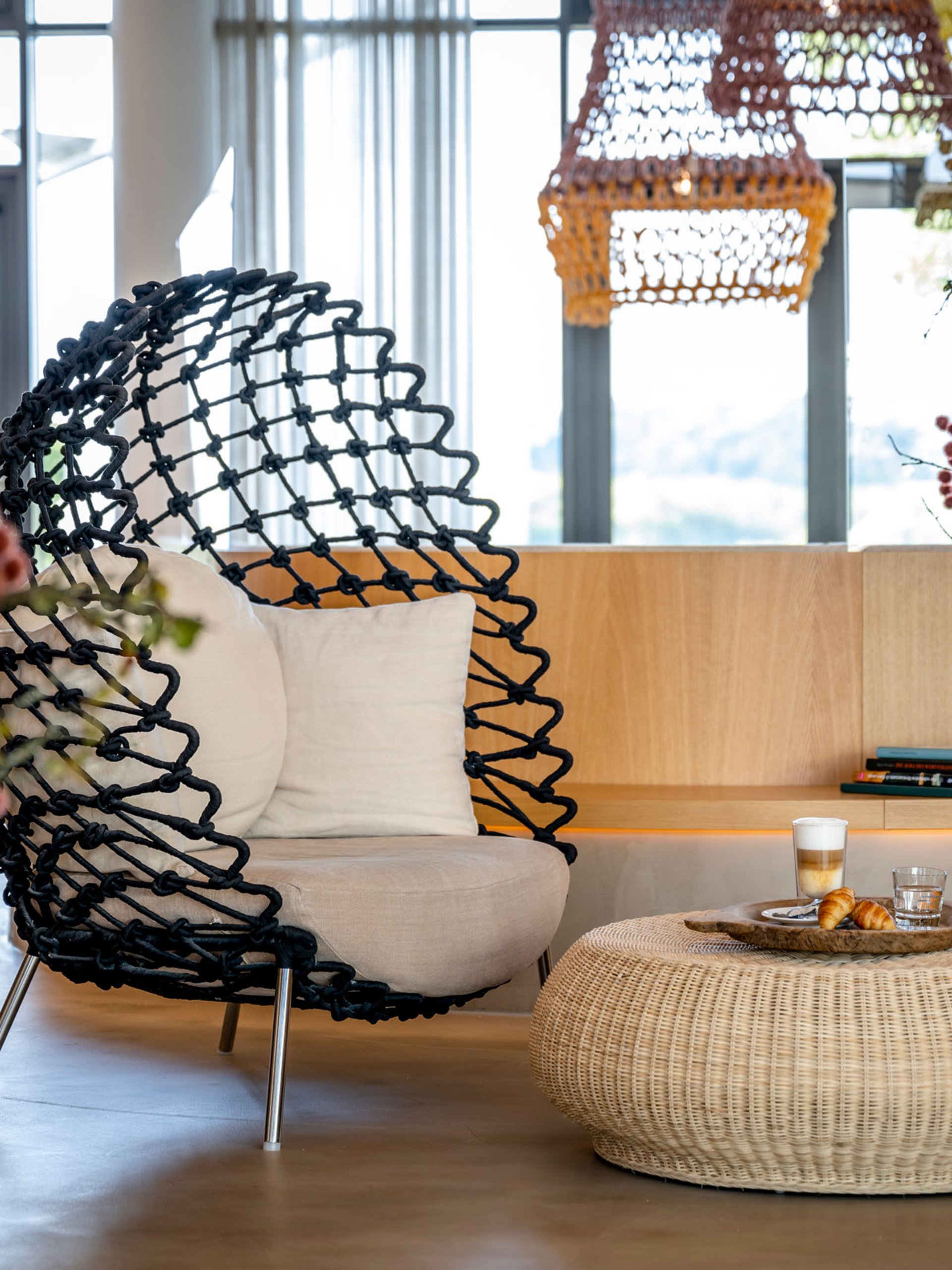 Espace salon moderne avec fauteuil noir, table en rotin et fleurs dans un salon lumineux