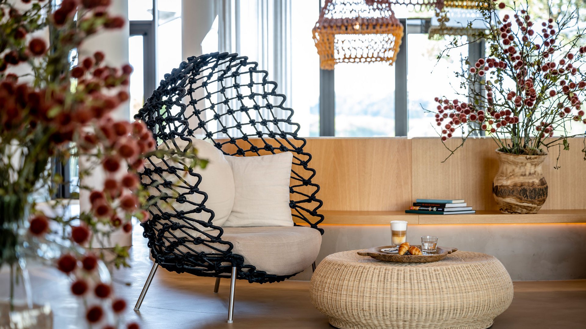 Moderner Sitzbereich mit Korbtisch, schwarzem Sessel und Blumen in einer hellen Lounge