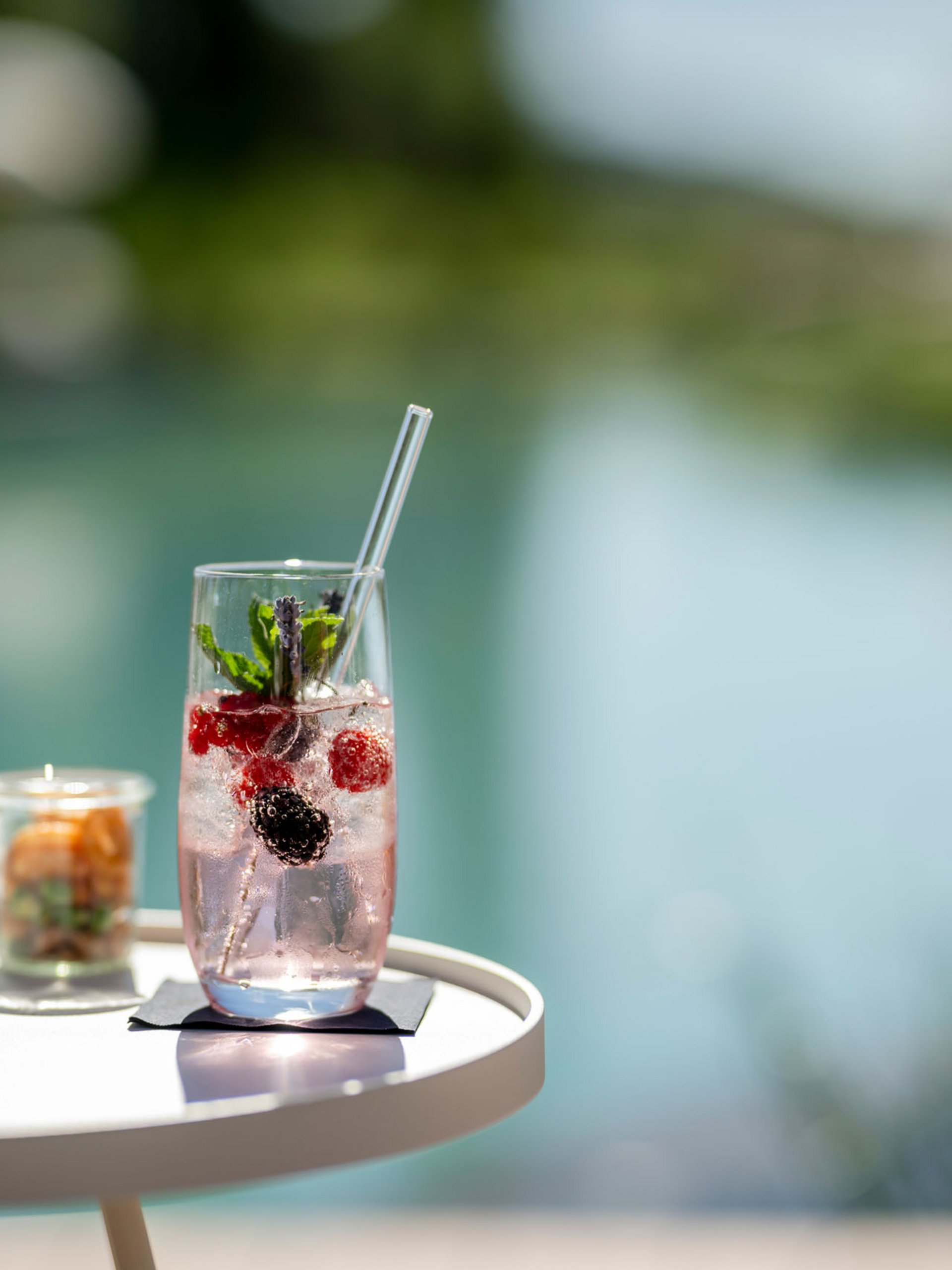Erfrischendes Getränk mit Beeren und Minze auf einem weißen Tisch am Wasser